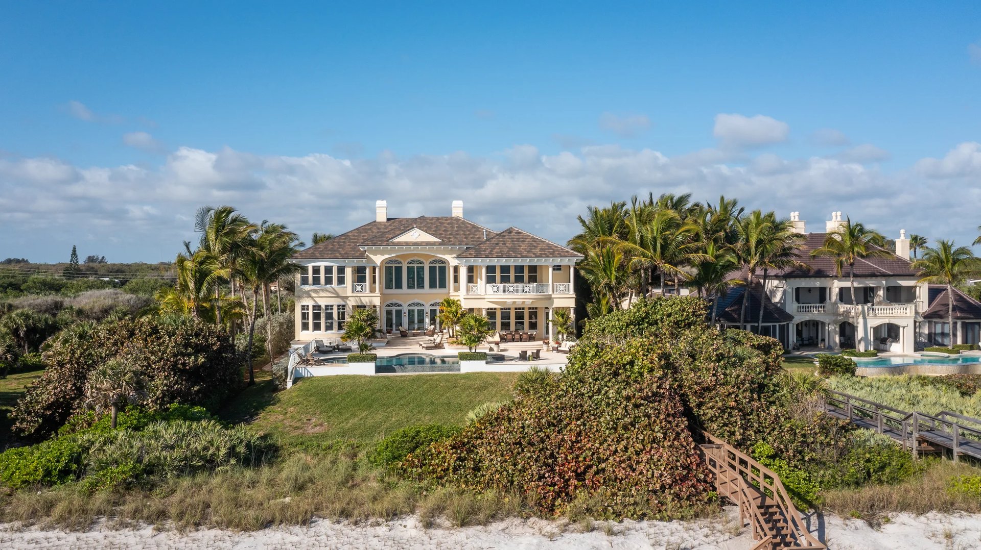 Aerial of an oceanfront estate showing the hipped terra-cotta roof, pool deck, and dune line