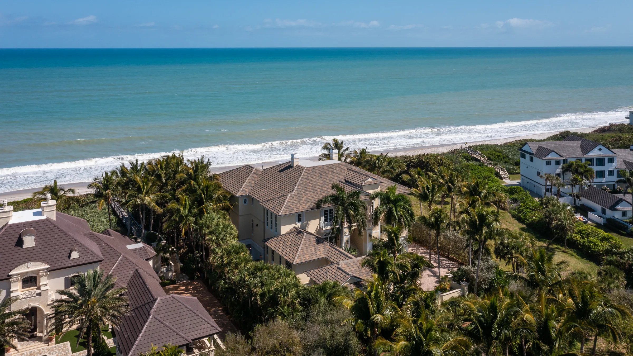 High aerial of 211 Beachside Drive showing the British West Indies estate, palm grounds, and turquoise Atlantic at Orchid Island