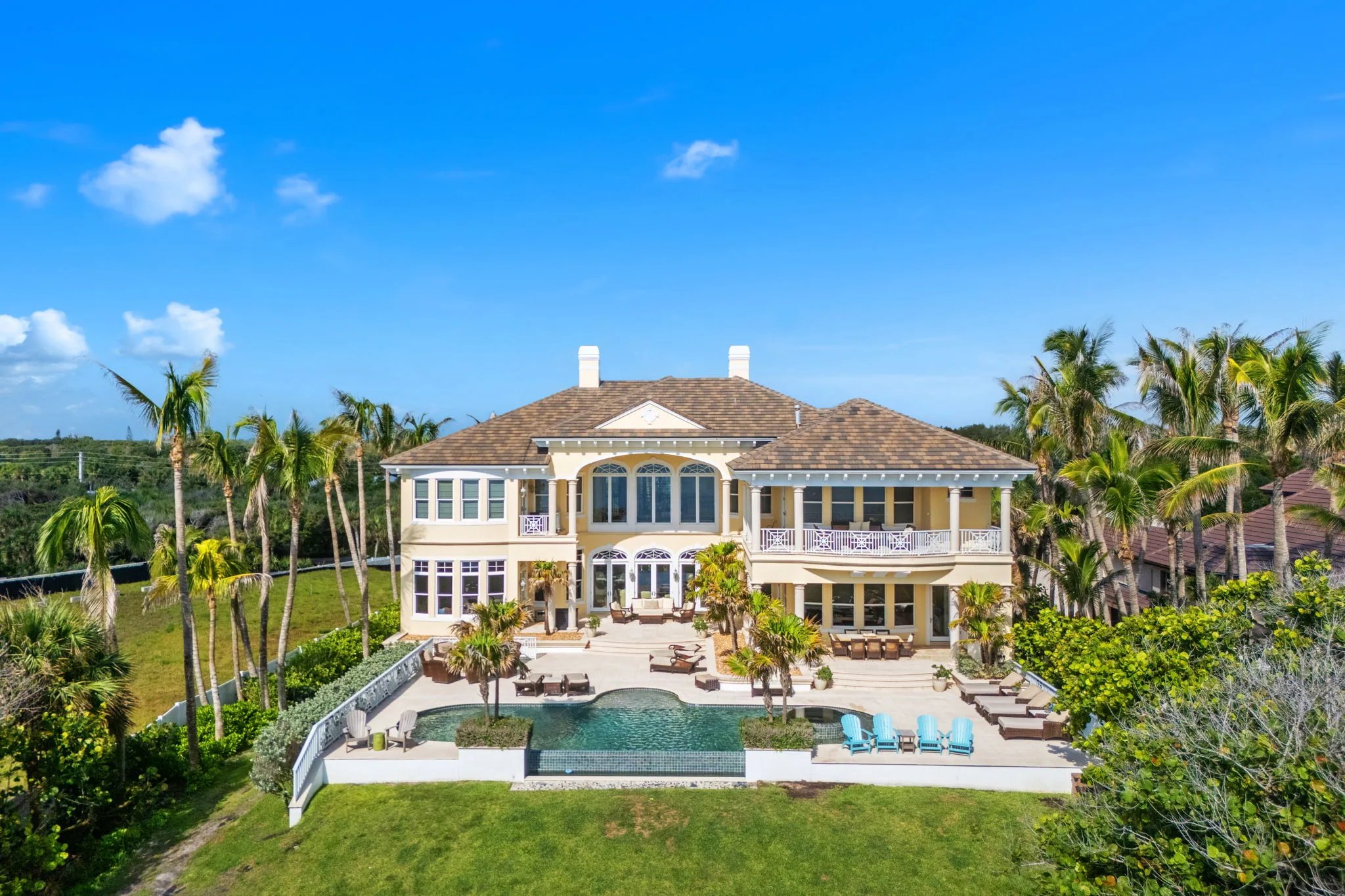 Centered aerial of the rear facade with infinity pool, palms, and oceanfront lawn at 211 Beachside Drive in Orchid