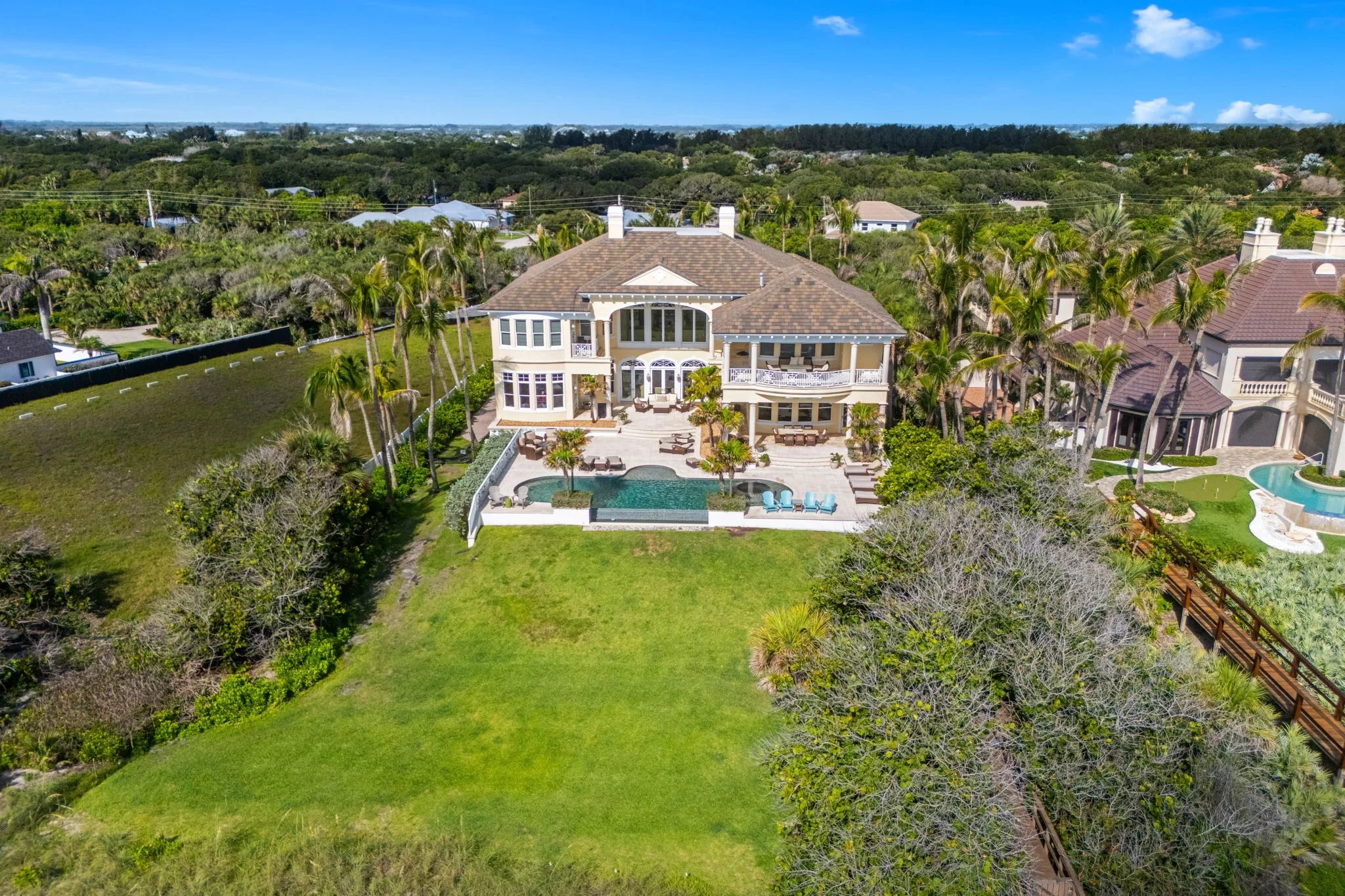 Aerial of the rear elevation showing infinity pool, oceanfront lawn, and the British West Indies architecture at 211 Beachside Drive