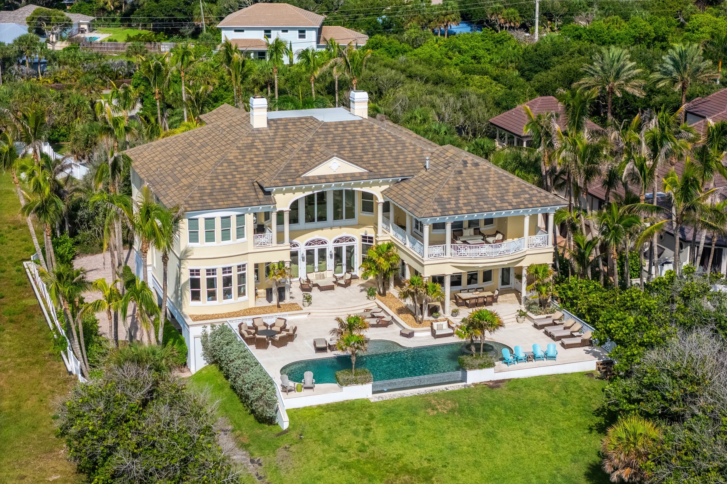 Aerial of British West Indies estate rooflines, twin chimneys and infinity pool nested in mature palms on Orchid, Florida