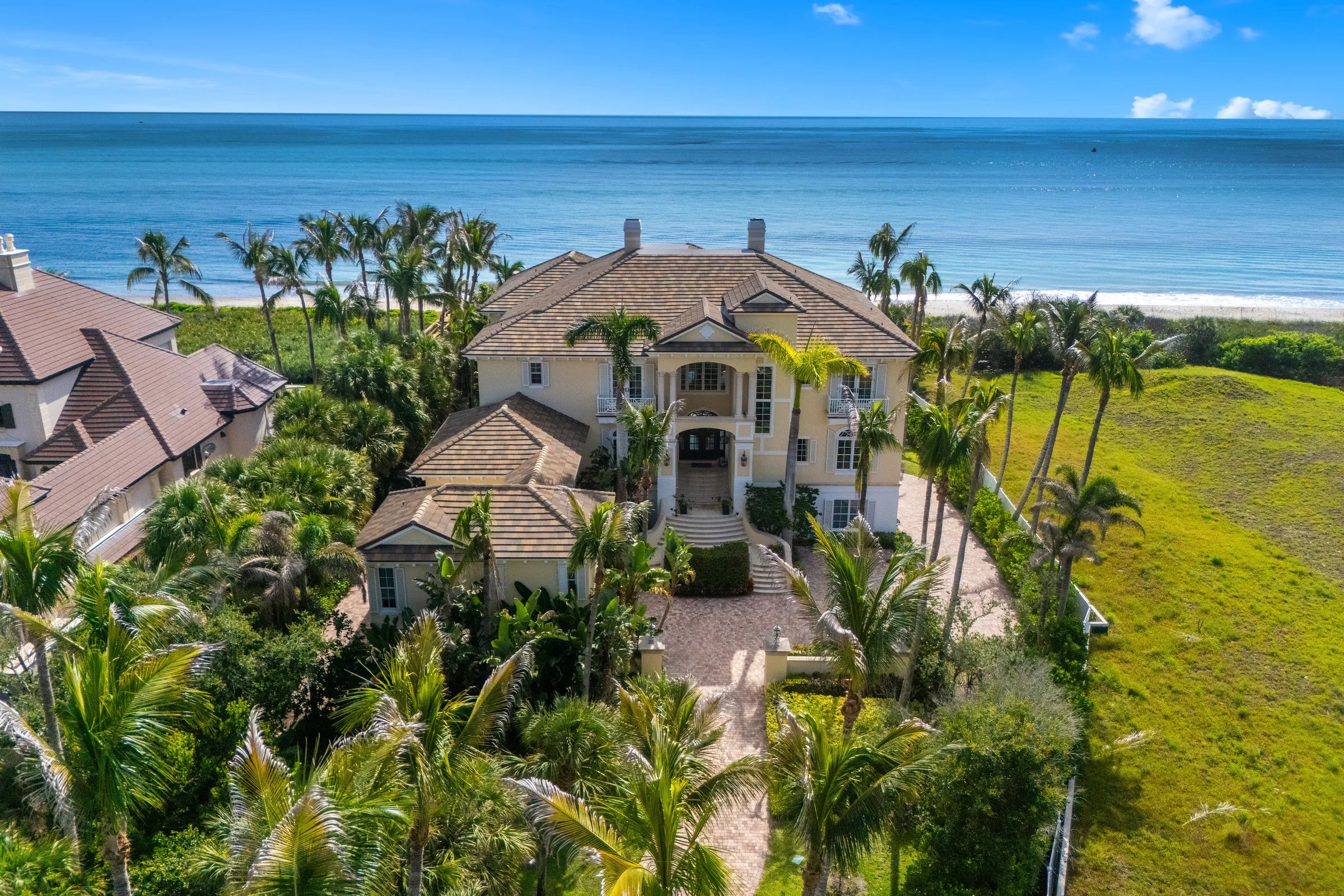 Aerial of the British West Indies estate at 211 Beachside Drive with palm-lined driveway and Atlantic shoreline beyond