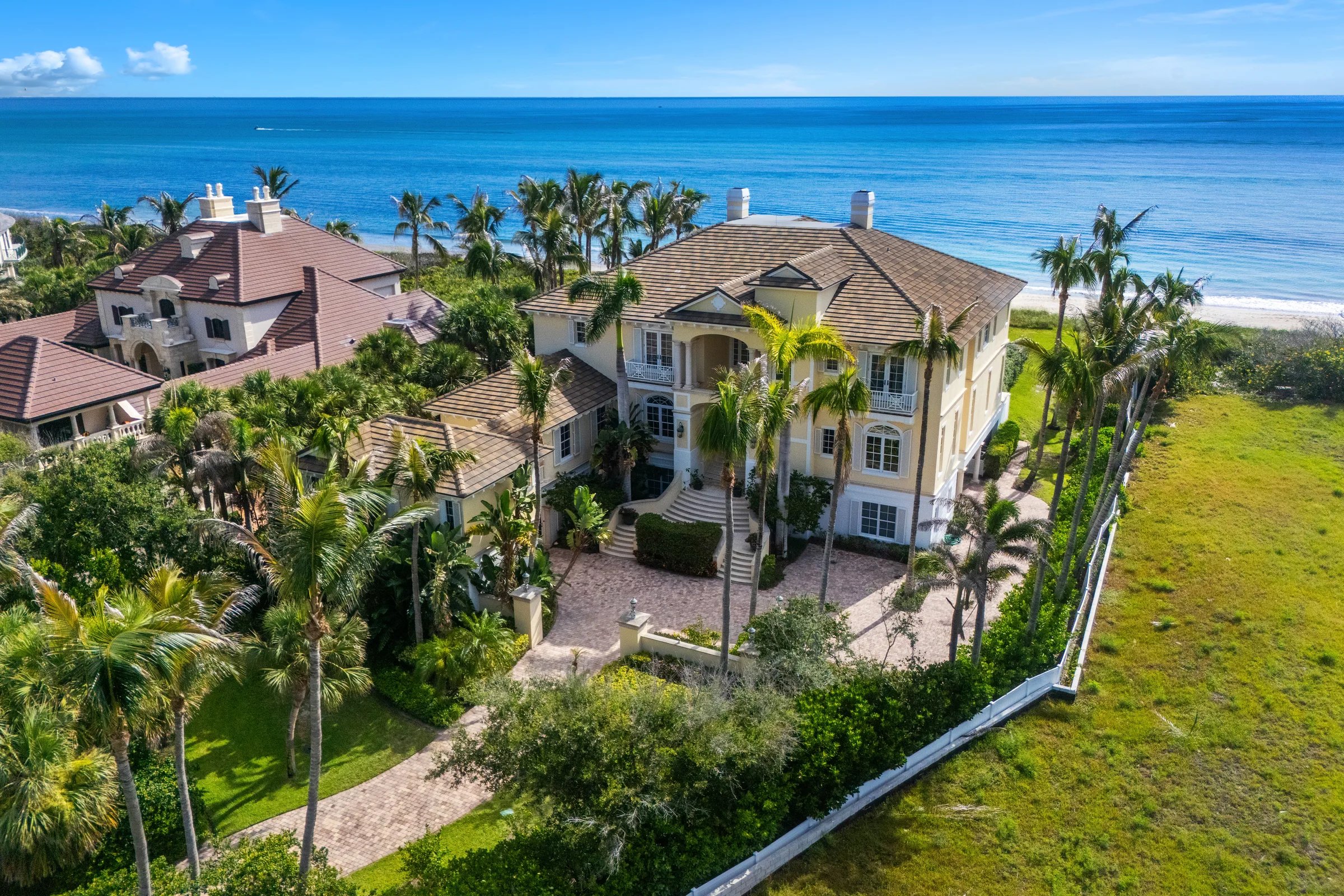 Drone view of the yellow estate with palm-shaded grounds set against the Atlantic horizon