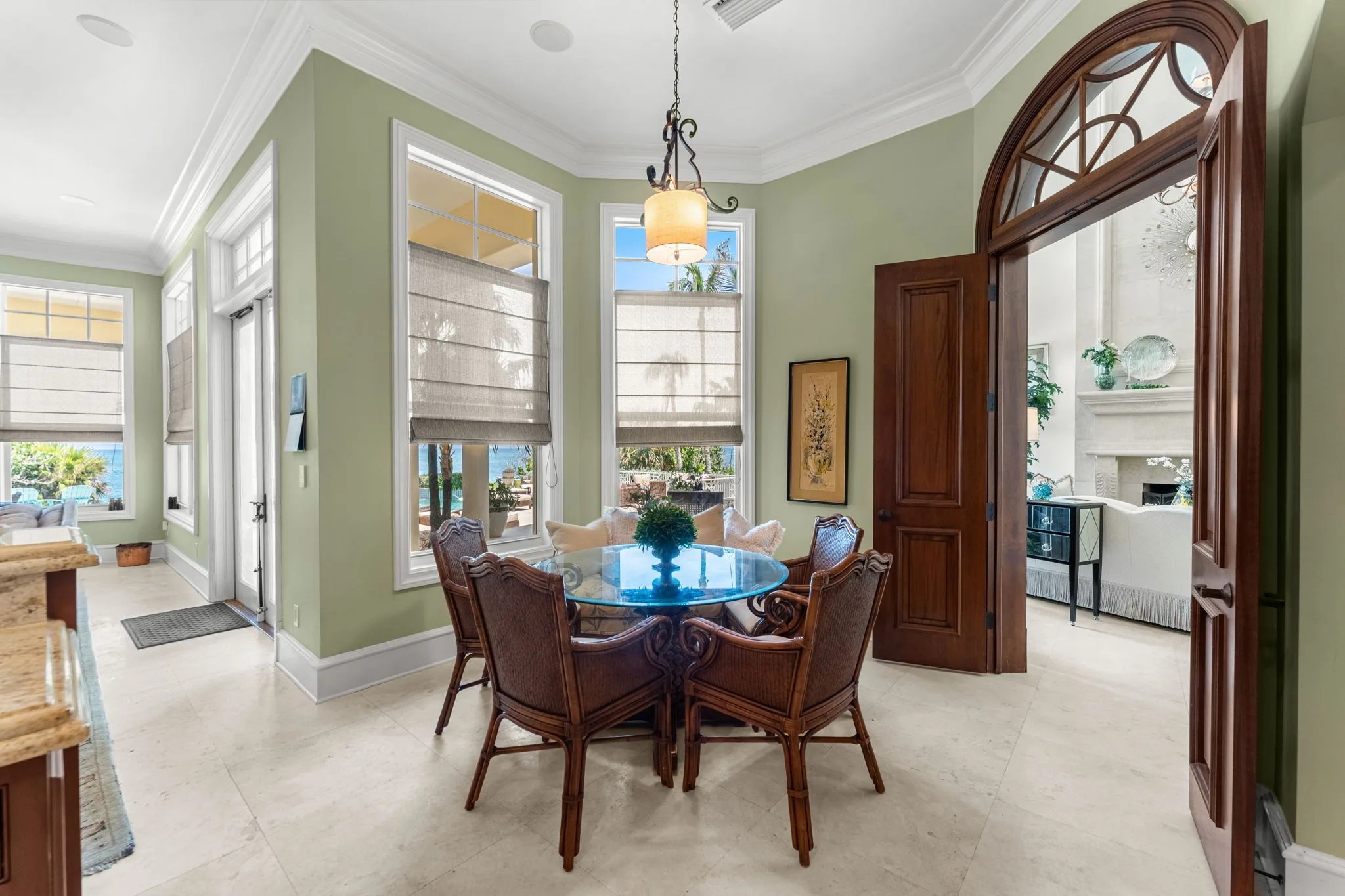 Breakfast nook with round glass table and rattan chairs framed by mahogany arched doorway to the great room