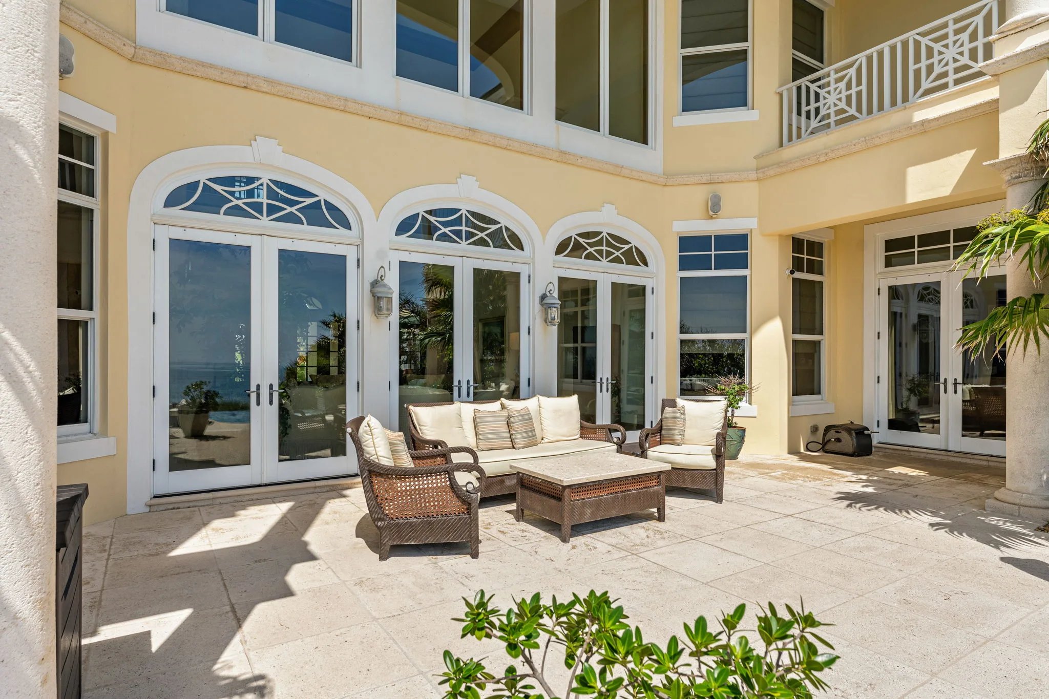 Sunlit courtyard ringed by tall arched French doors with wicker seating beneath the second-floor lanai