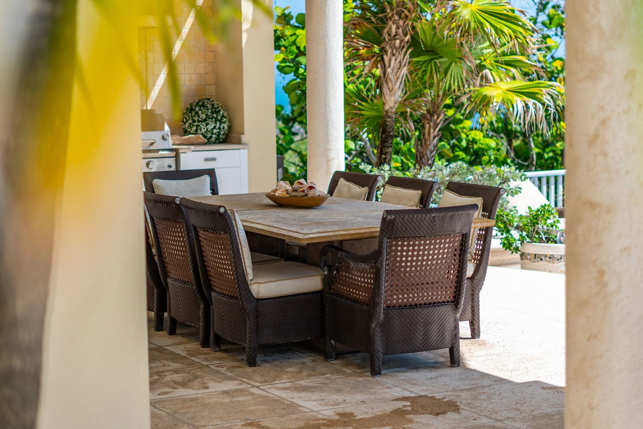 Detailed view of outdoor wicker dining table with shells centerpiece beside the summer kitchen on the covered lanai