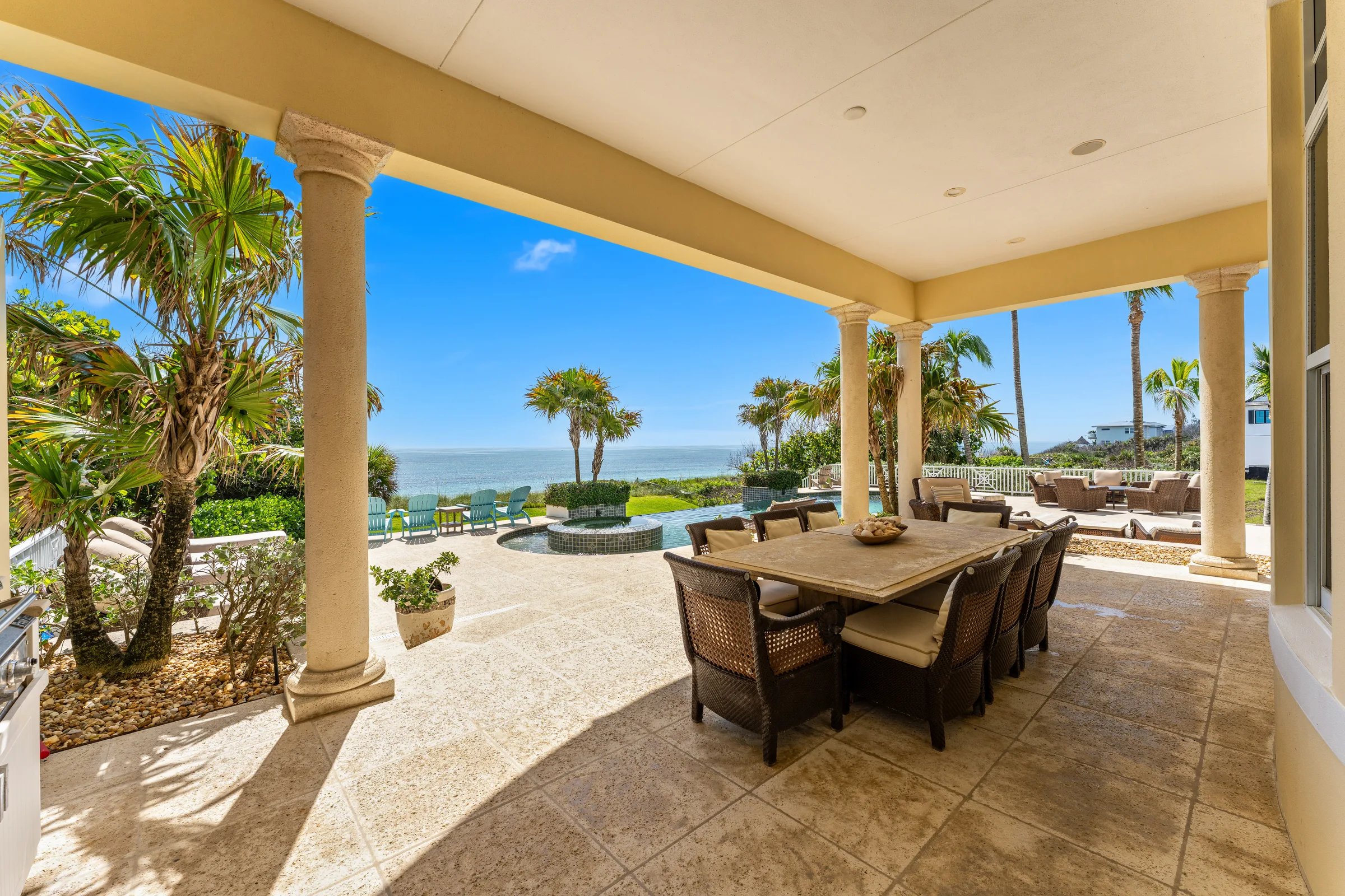 Covered oceanfront lanai dining table framed by stone columns overlooking infinity pool and Atlantic horizon
