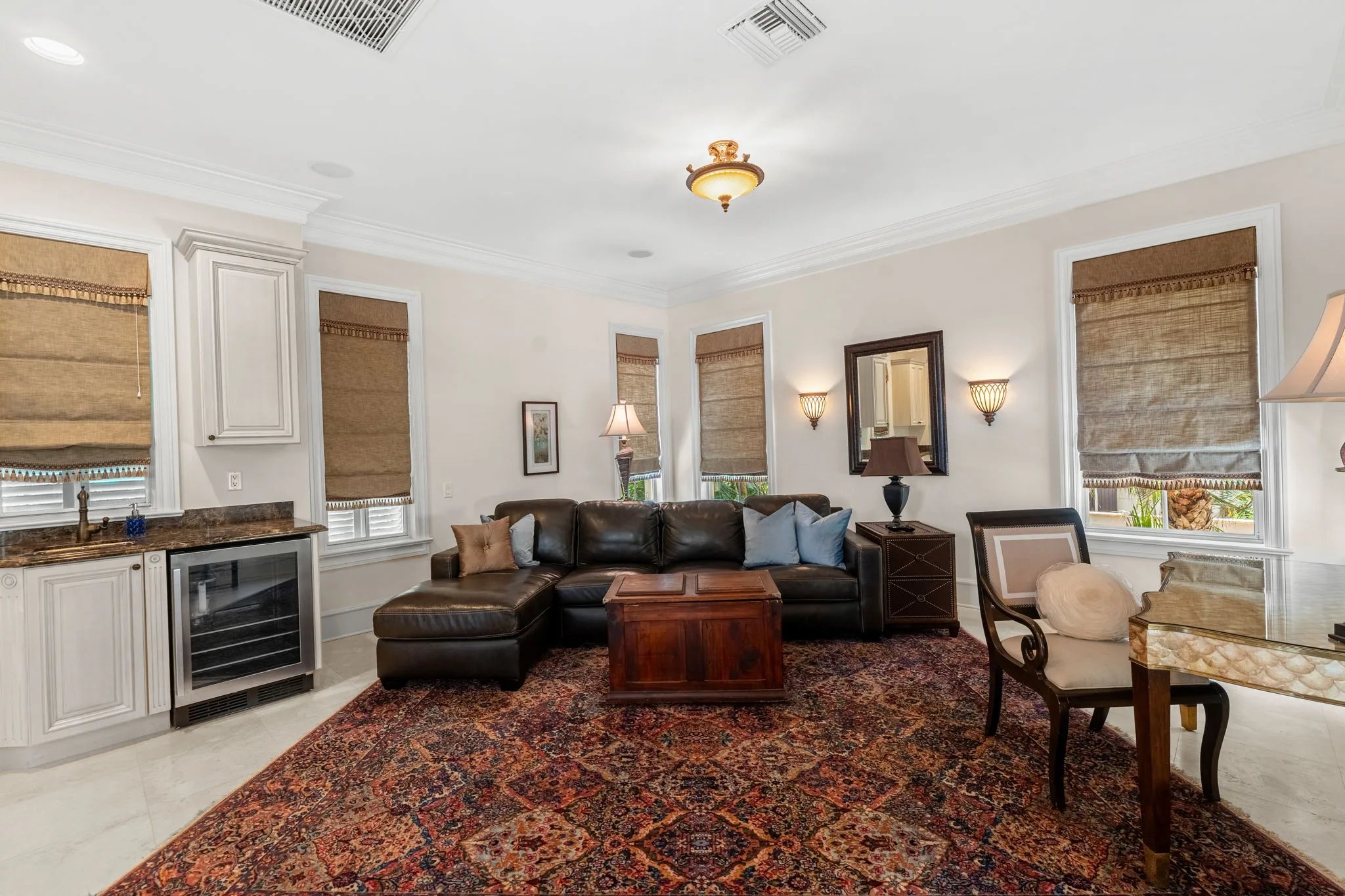 Leather sectional and wine fridge nook anchor the den beside woven roman shades