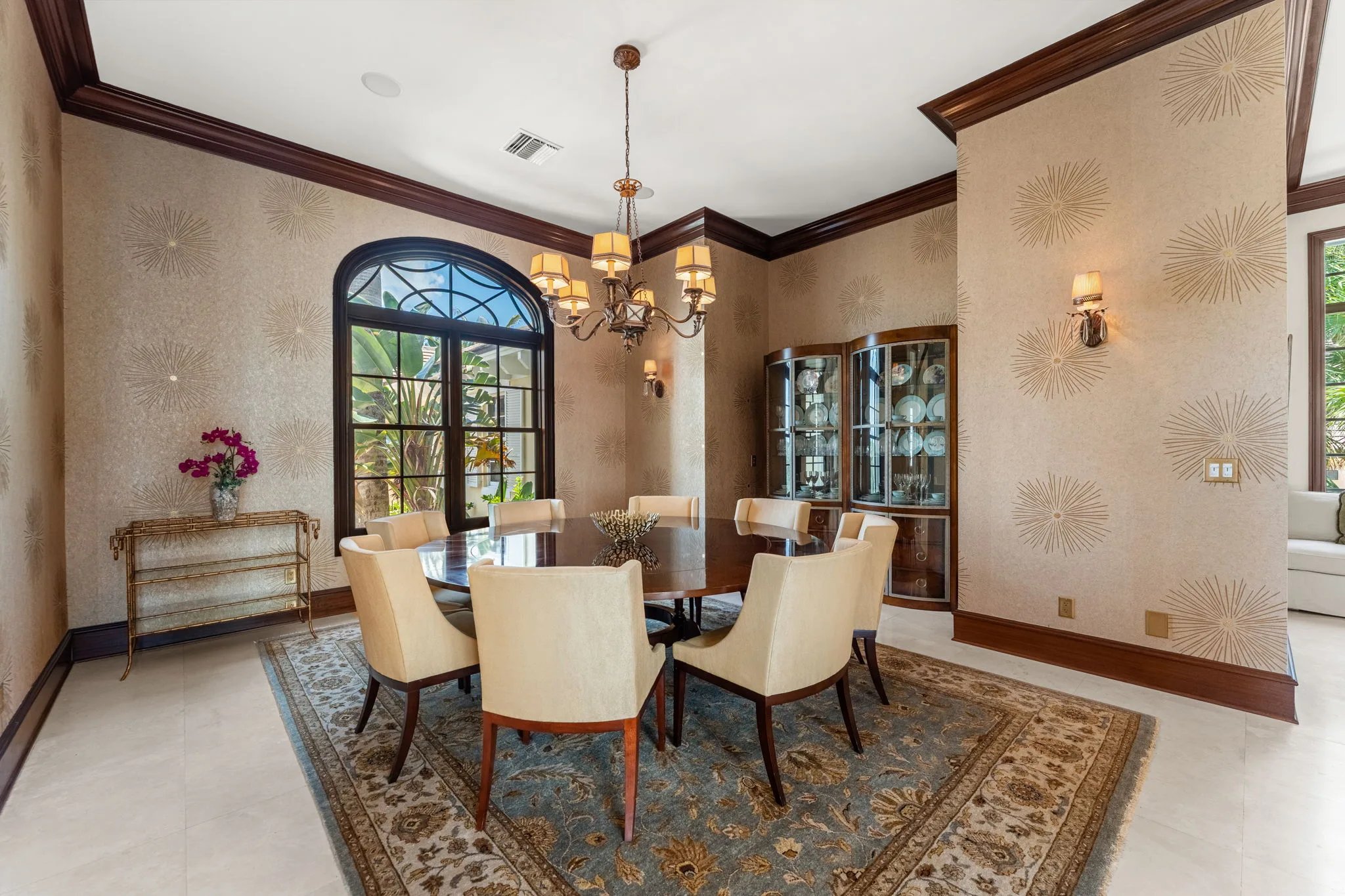 Formal dining with starburst chandelier, mahogany table, and arched window beyond