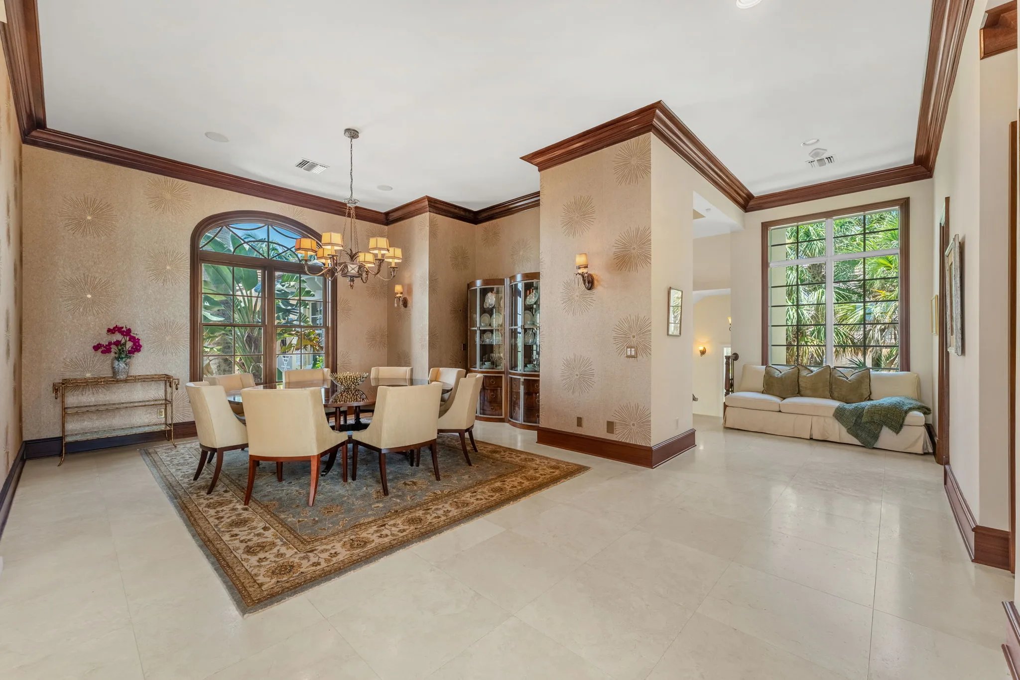Formal dining room with mahogany table, upholstered chairs, brass chandelier and patterned wallpaper