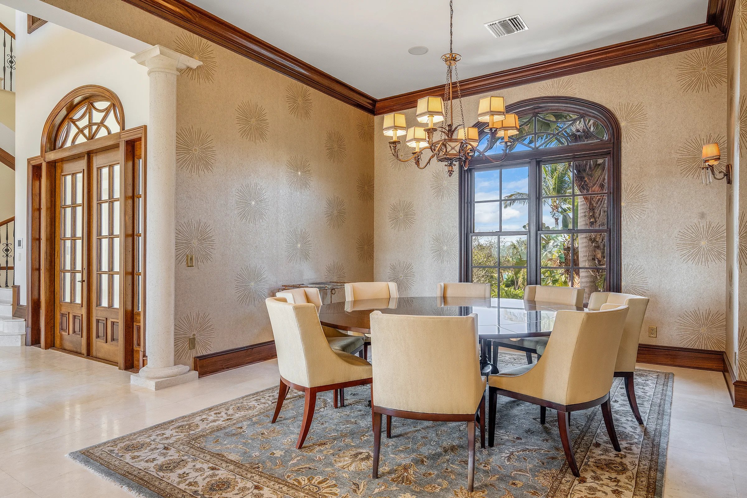 Formal dining room with chandelier, upholstered chairs, arched window, and patterned wallpaper
