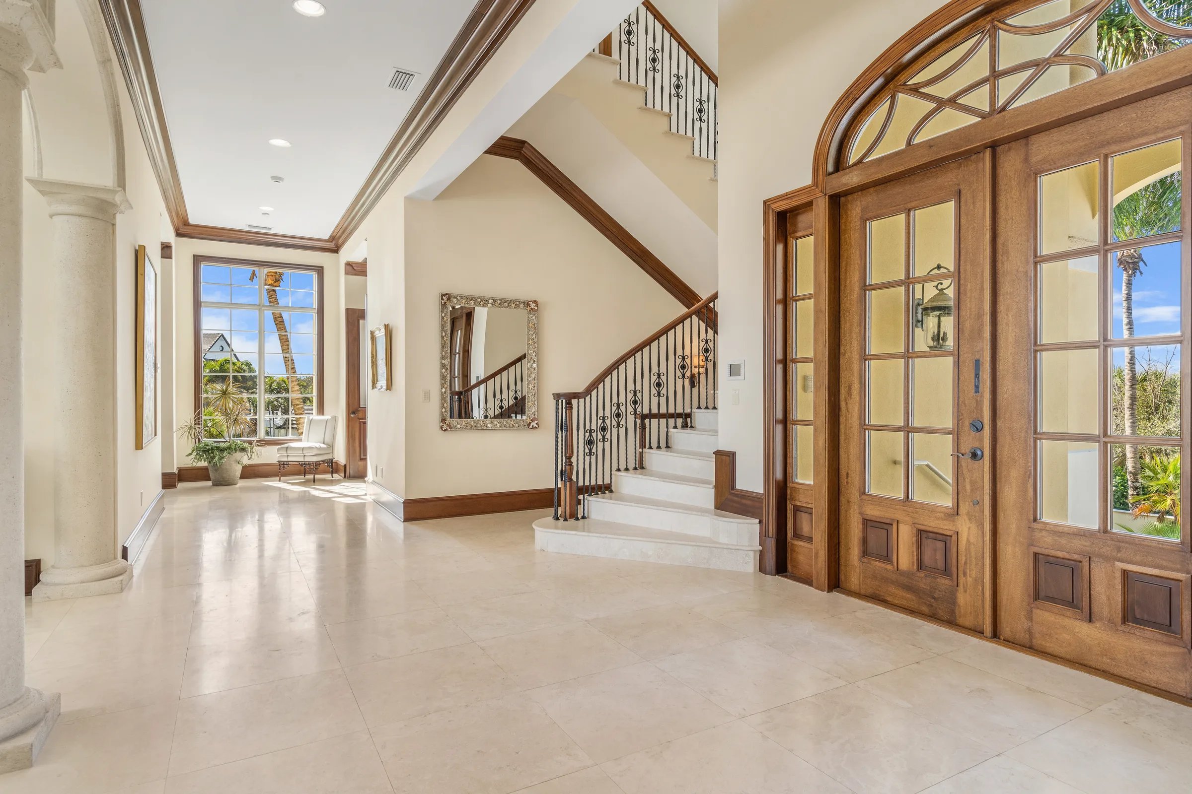 Wide front foyer with classical columns, marble floors, and arched mahogany doors at 211 Beachside Drive in Orchid