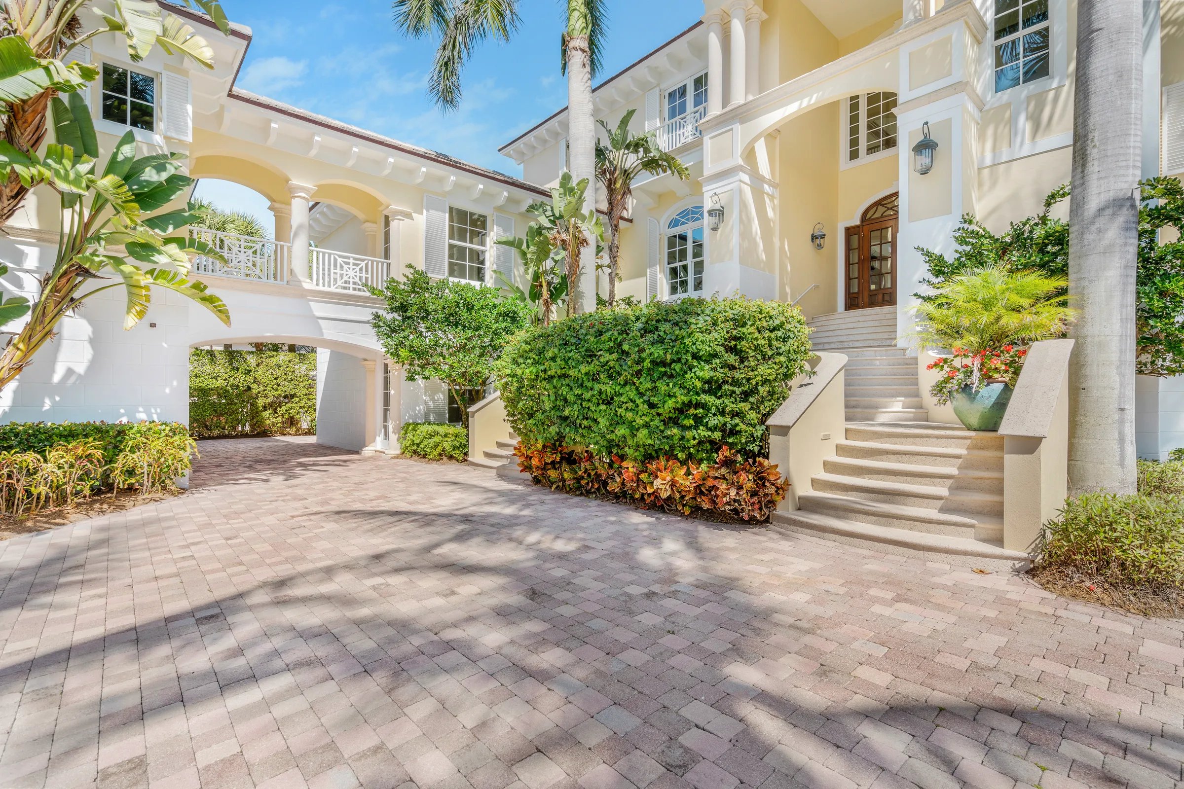 Side approach to 211 Beachside Drive with paver motor court, porte-cochere passage, and the entry steps to the mahogany doors