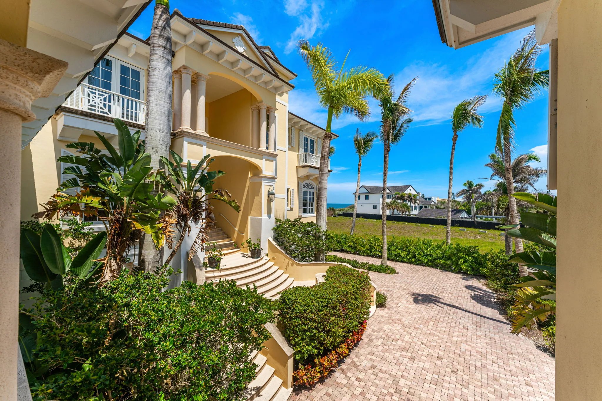 Curved entry staircase between pediment portico and brick drive with bird-of-paradise palms