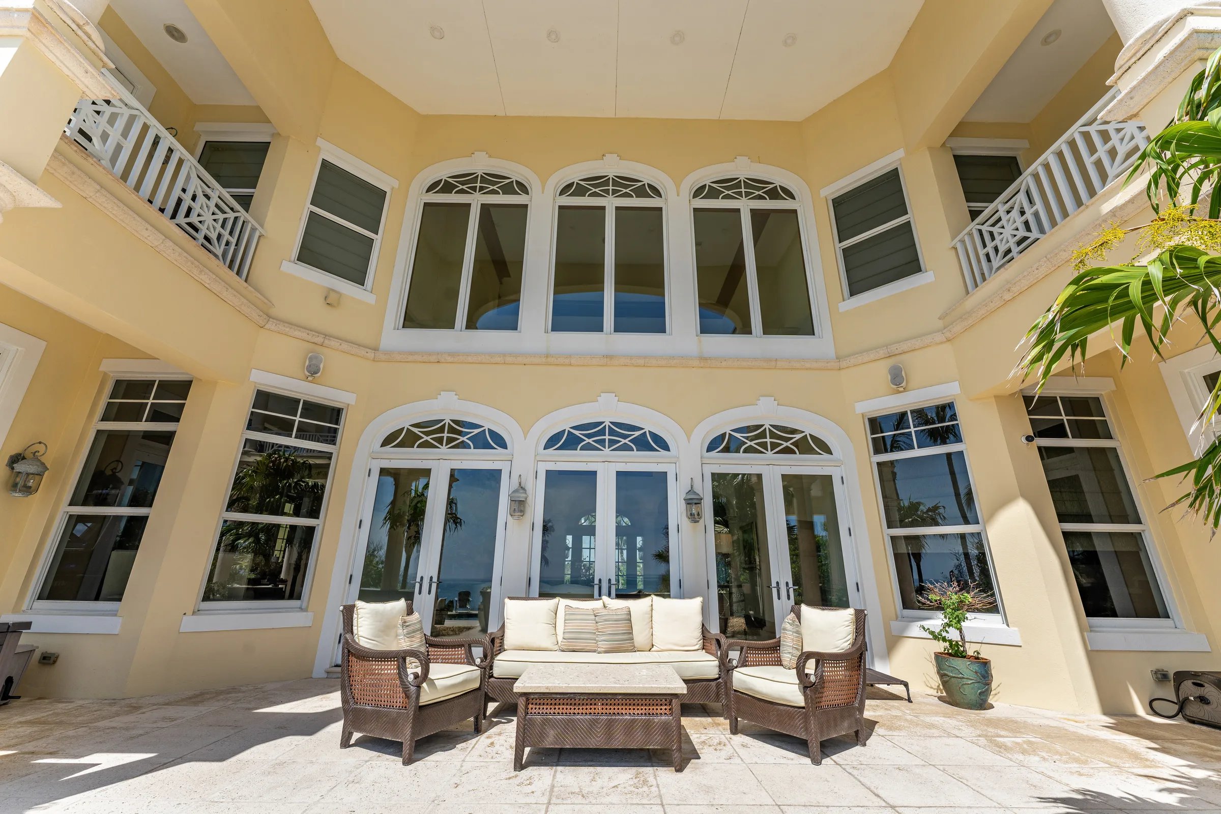 Rear facade with two-story arched windows, classical balconies, and travertine terrace seating in Orchid, Florida