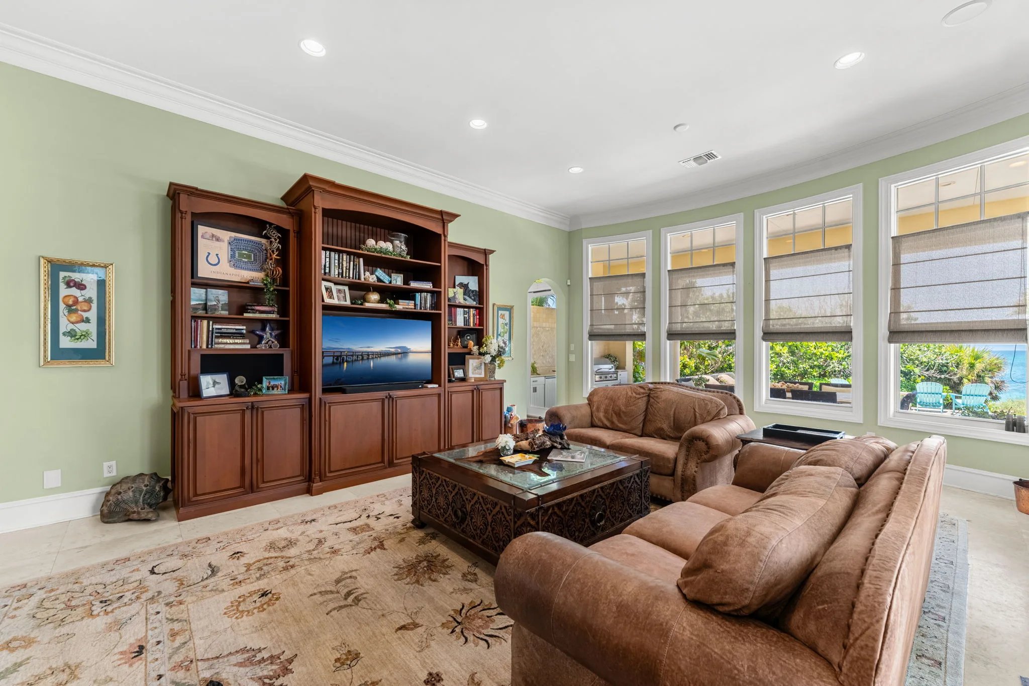 Family room in sage green with leather sofas, built-in media wall and ocean view through tall windows