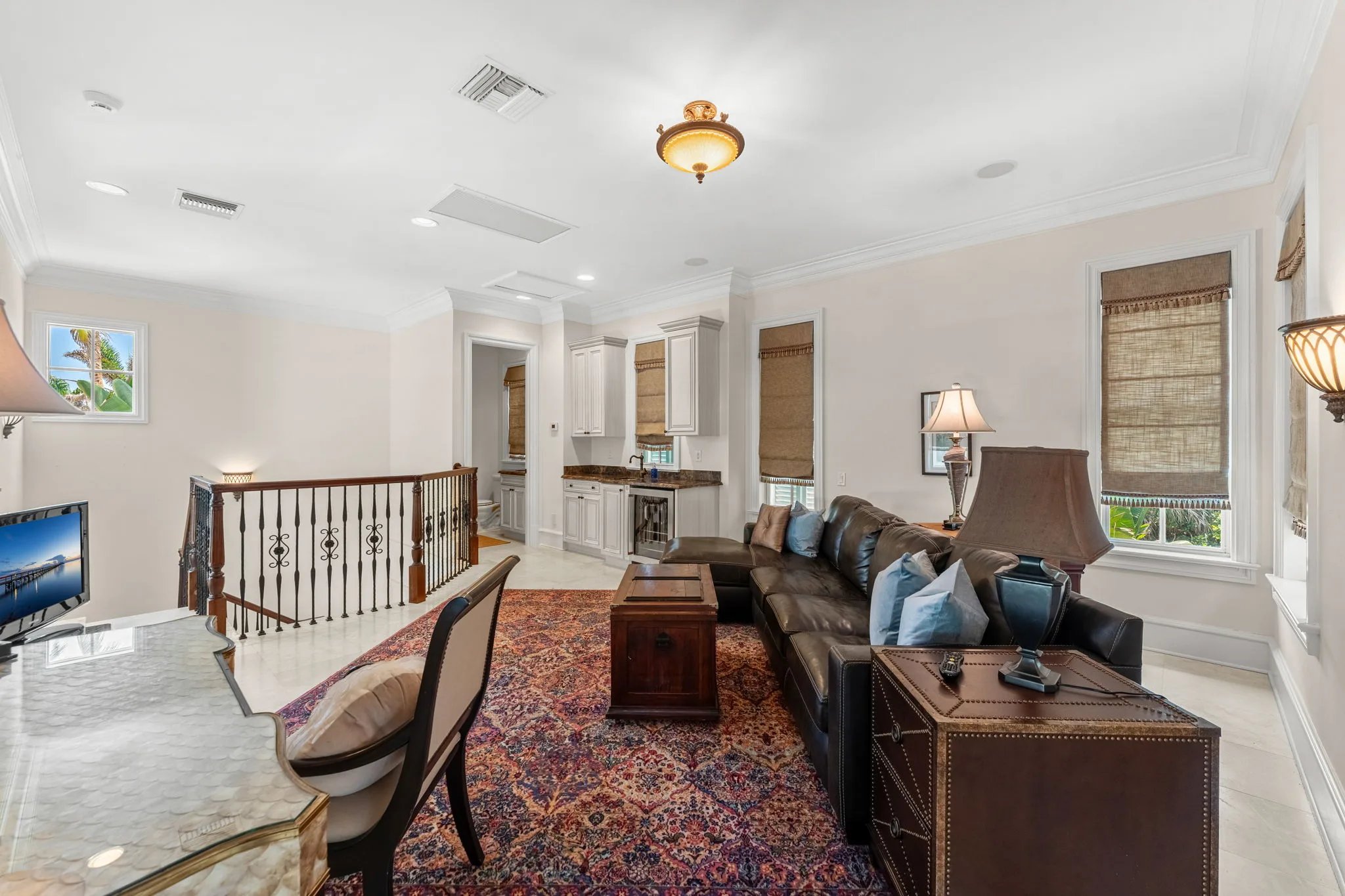Upper-level gallery landing with leather sectional, wet bar and wrought-iron balustrade above the foyer