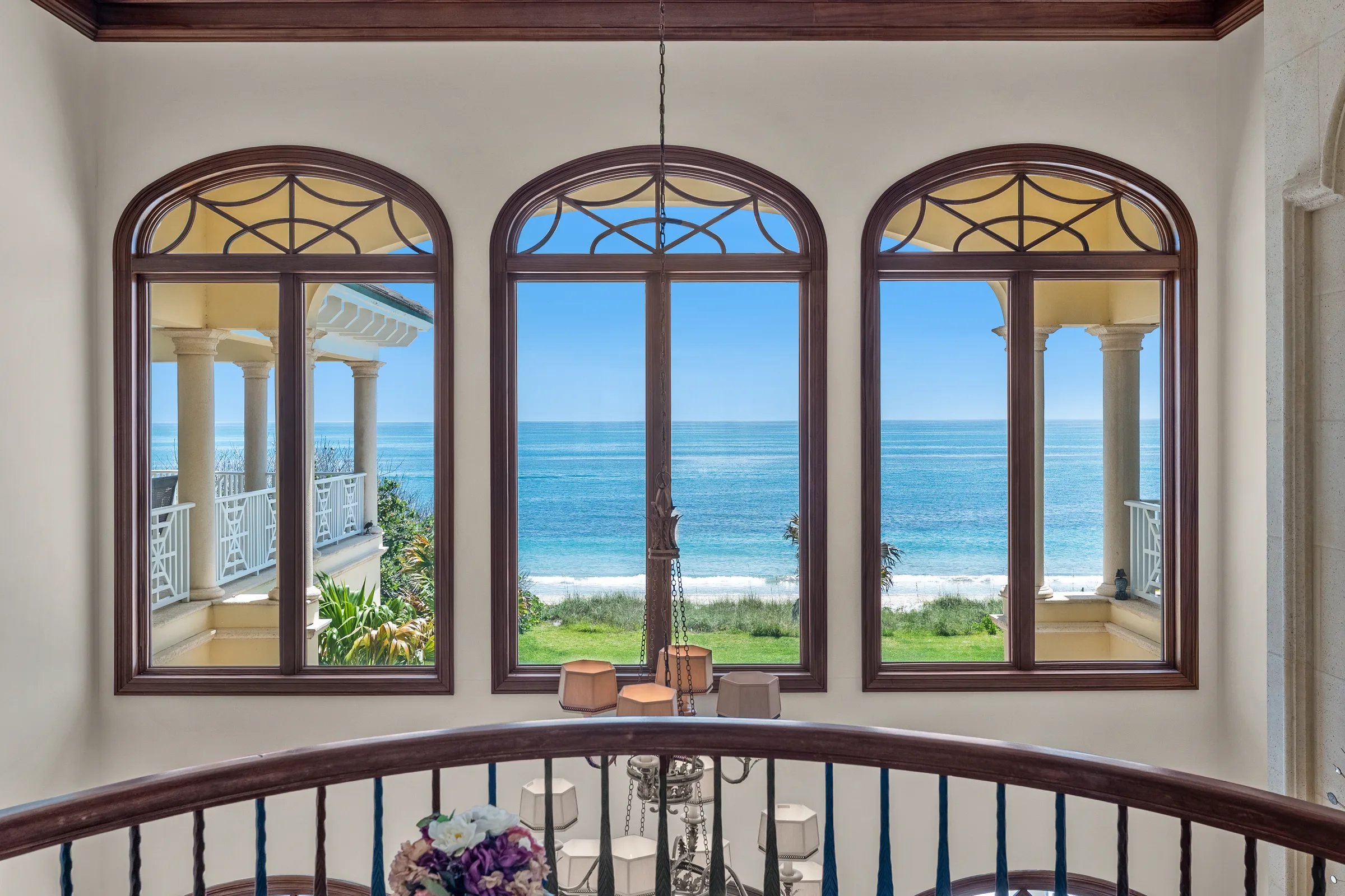 Three arched windows framing turquoise Atlantic horizon above curved iron staircase rail