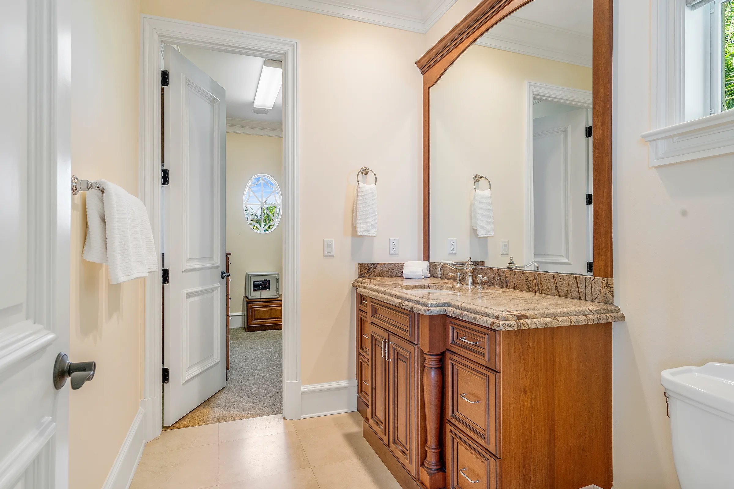 Guest bath with cherry vanity, rainforest-marble counter, and tall arched mirror, doorway opening to an adjoining sitting room