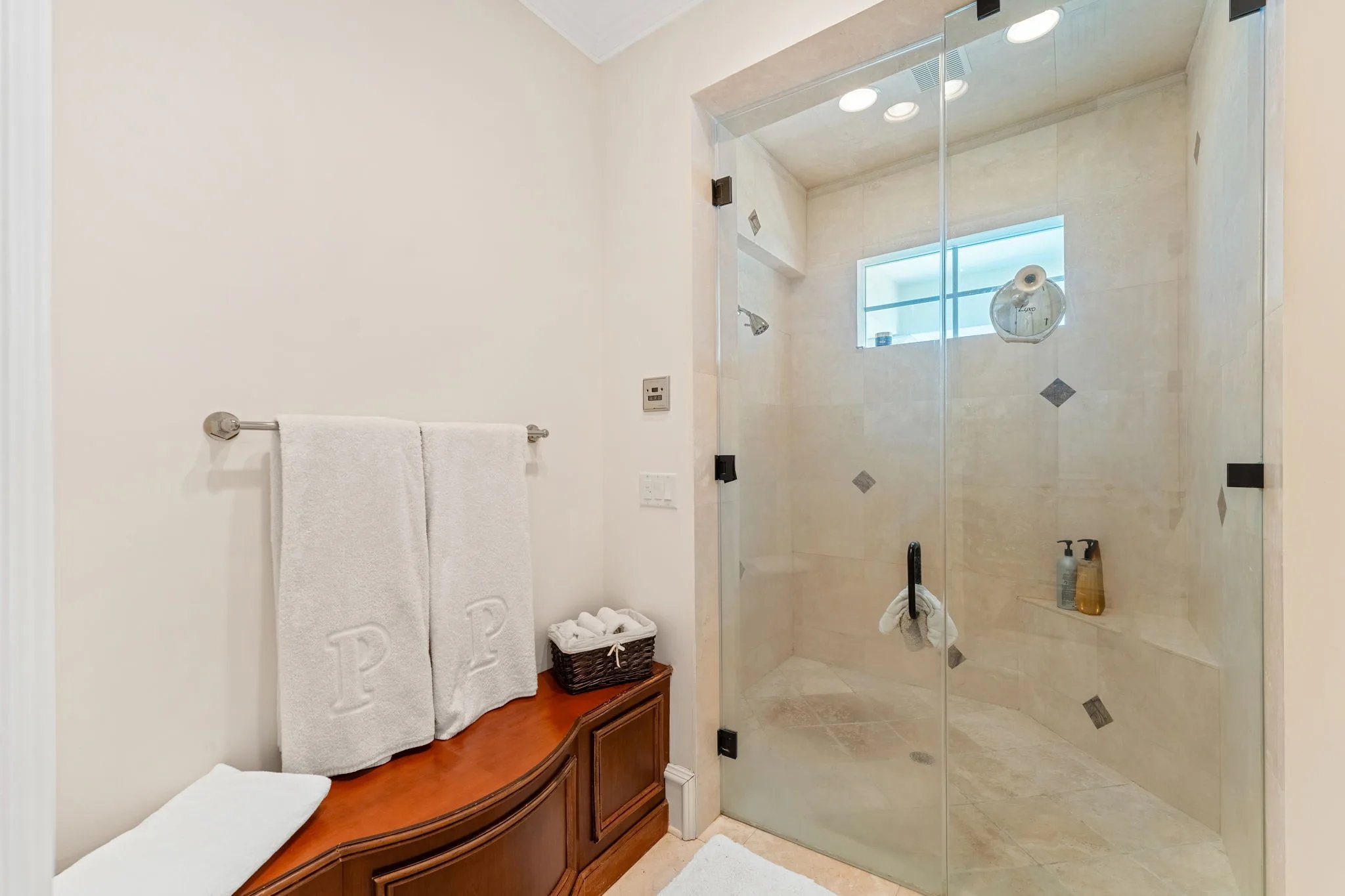 Guest bath with double-head walk-in glass shower, monogrammed towels, and cherry storage bench