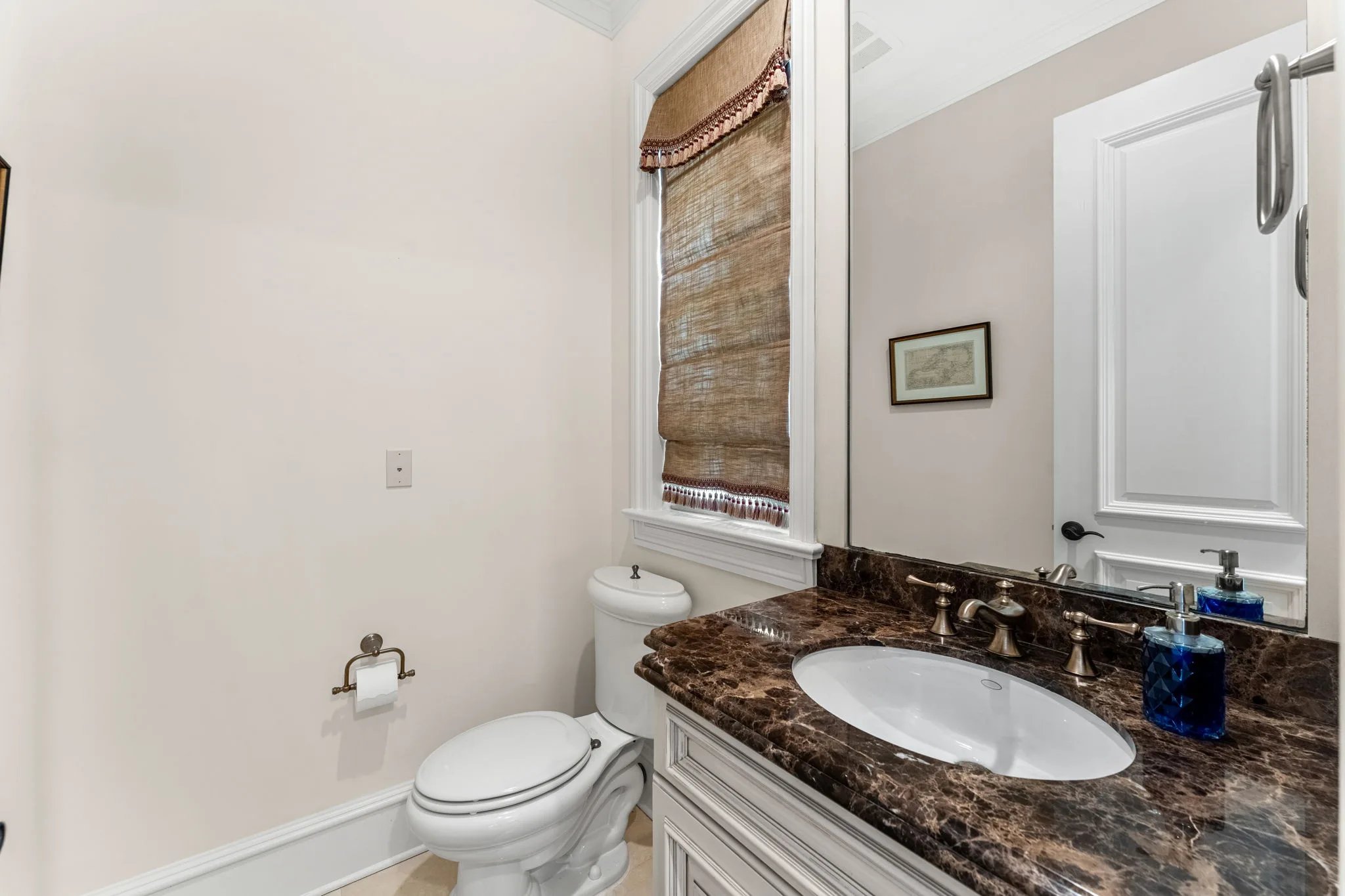 Guest bath with dark emperador marble vanity, blue glass accents and palm-shaded window