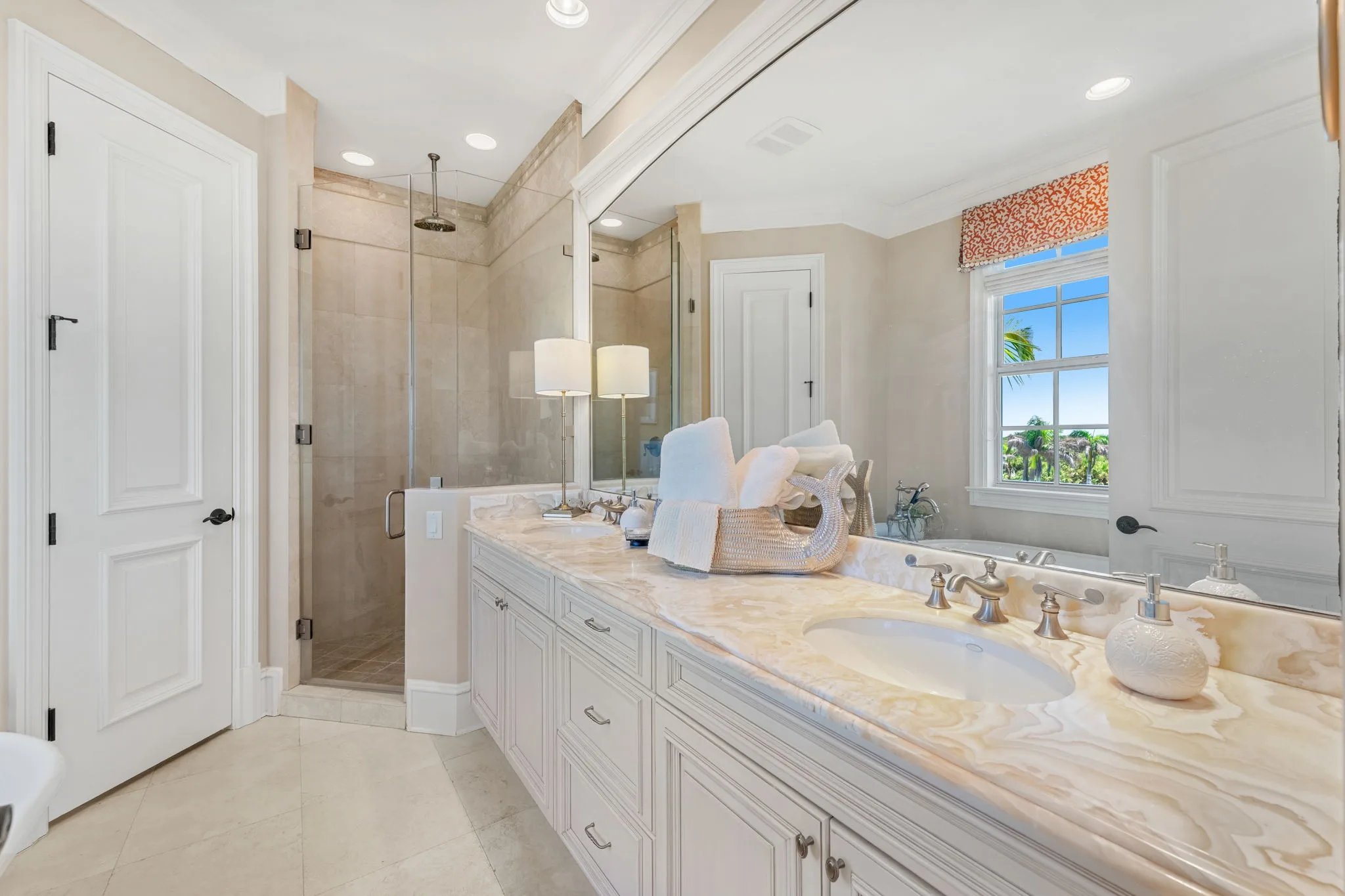 Guest bath with onyx double vanity, glass shower, and coral roman shade