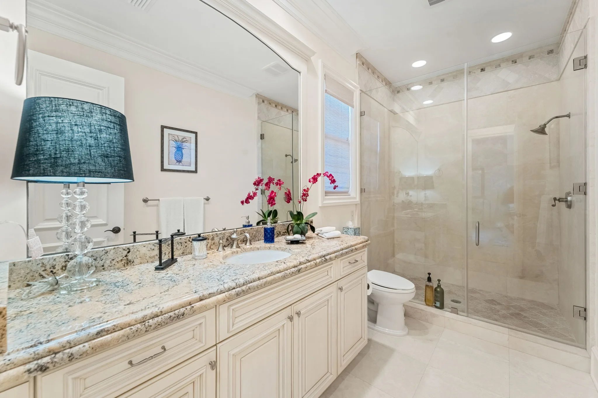 Guest bath with granite vanity, glass walk-in shower, and pineapple coastal artwork