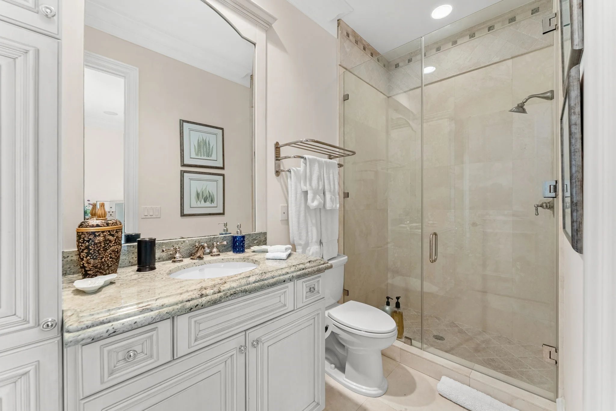 Guest bath with granite vanity, framed botanical prints, and glass-enclosed travertine shower