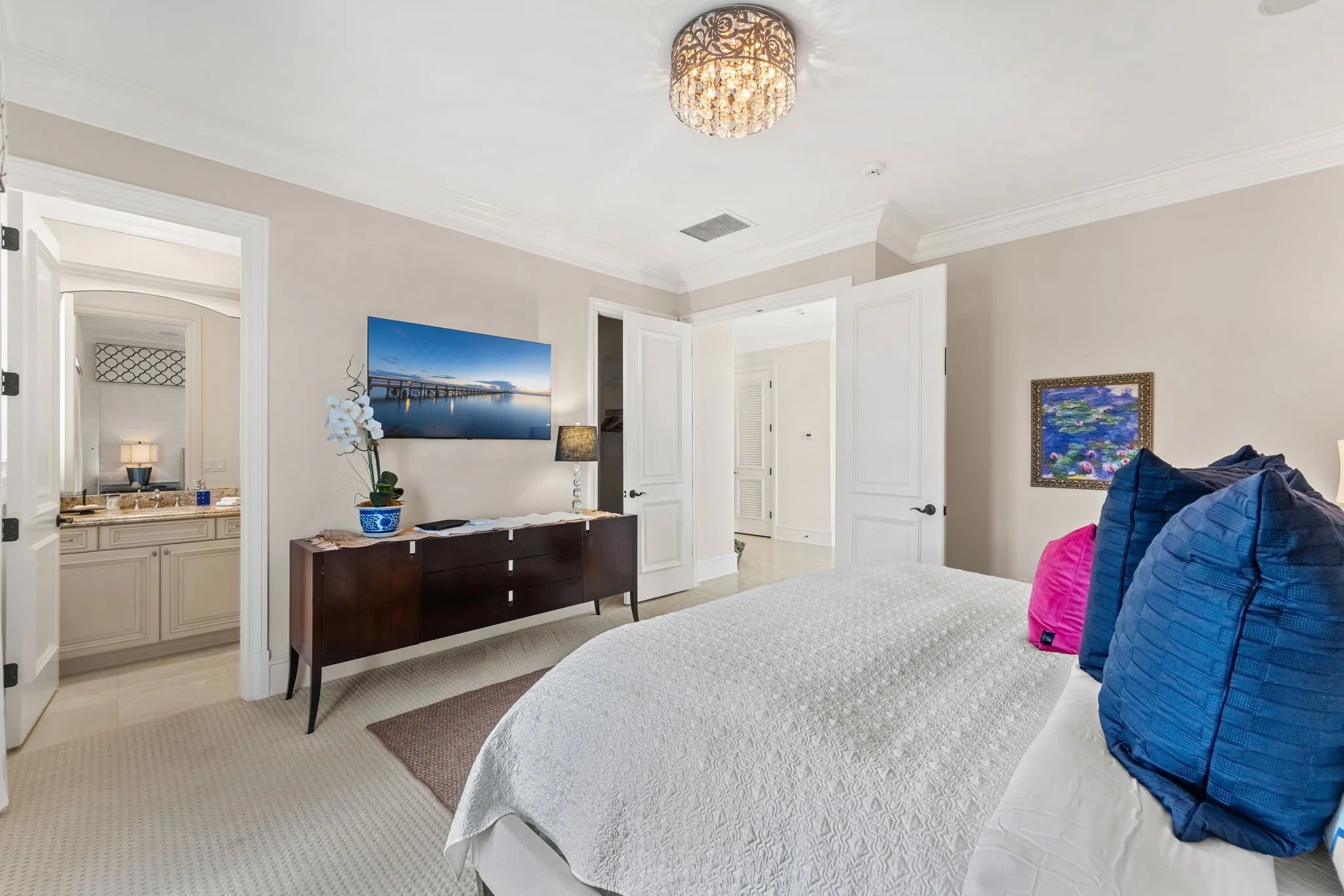 Guest bedroom with crystal flush-mount chandelier, dresser, and ensuite doorway