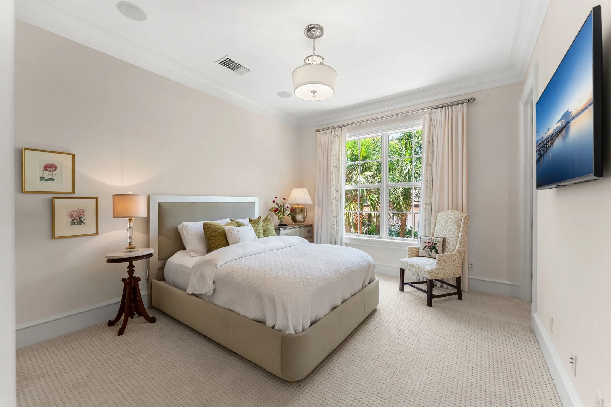 Guest bedroom with upholstered king bed, green accent pillows and tall palm view through bayfront window