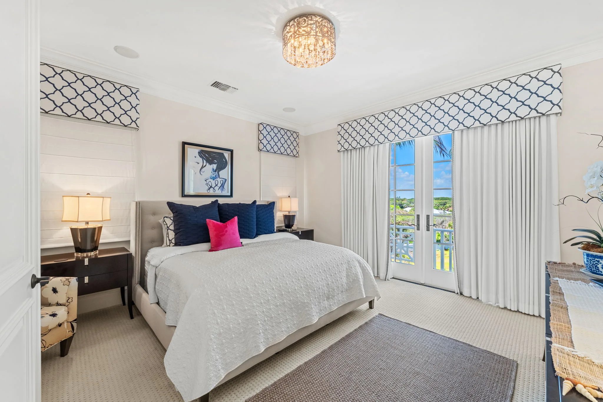 Navy and pink pillows accent a guest bed beside French doors near the Atlantic