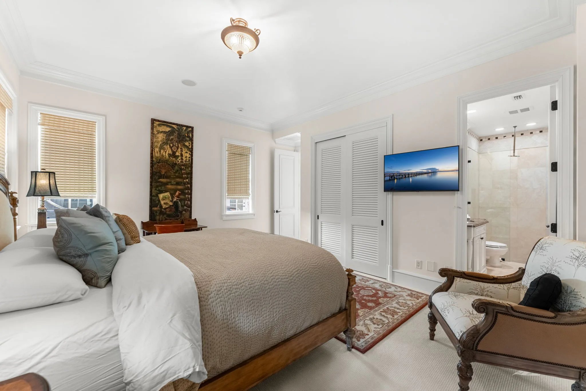 Guest bedroom with king bed, framed botanical scroll and ensuite bath beyond louvered closet doors