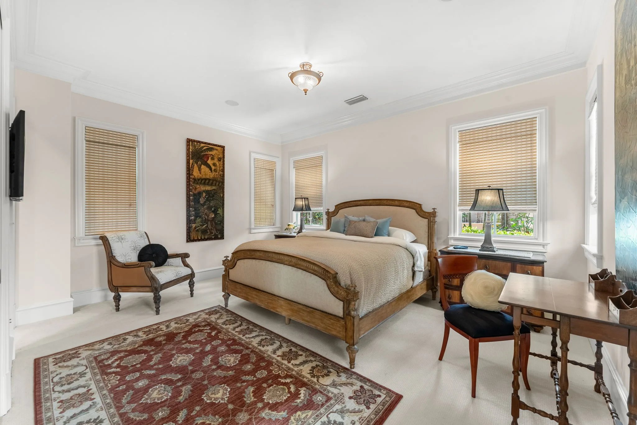 Carved king bed and tropical tapestry sit between shaded windows in a guest suite