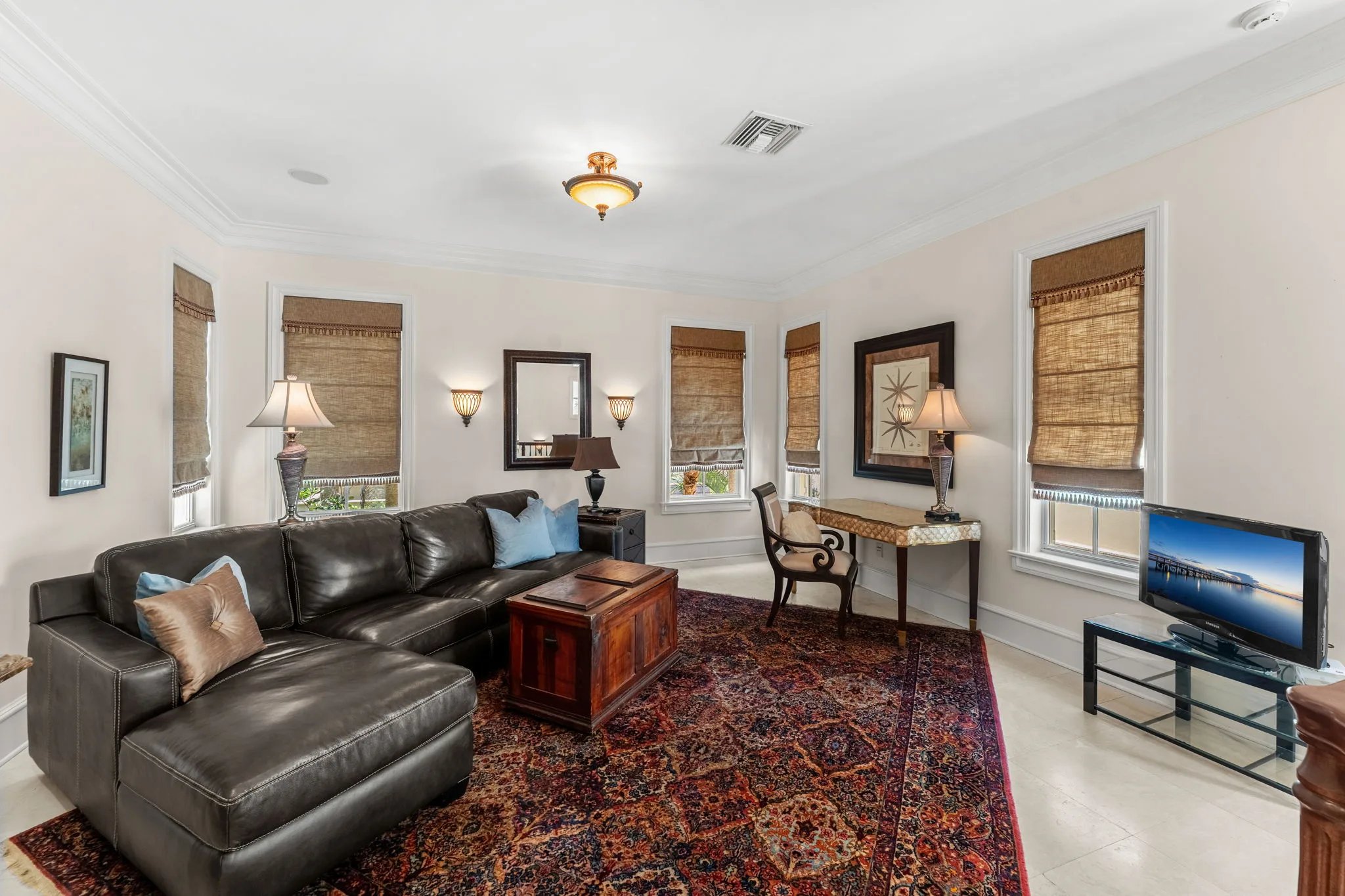 Guest sitting room with leather sectional, persian rug, and roman shades