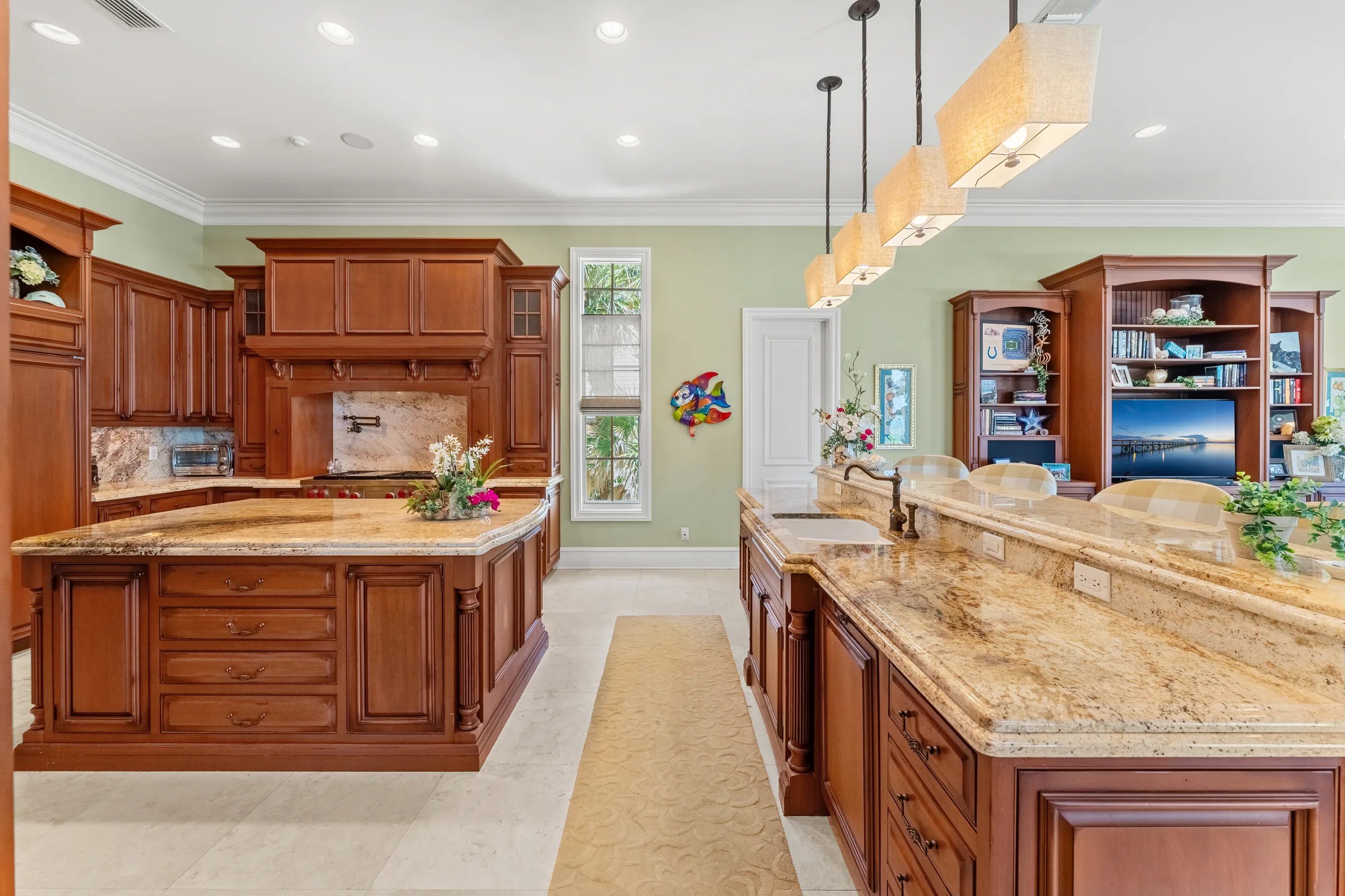 Chef kitchen with twin granite islands, cherry cabinetry, and warm pendant lighting