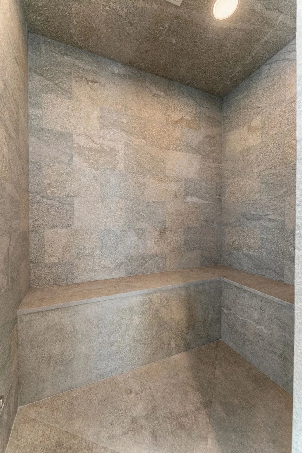 Stone-tiled shower interior with built-in bench and recessed lighting