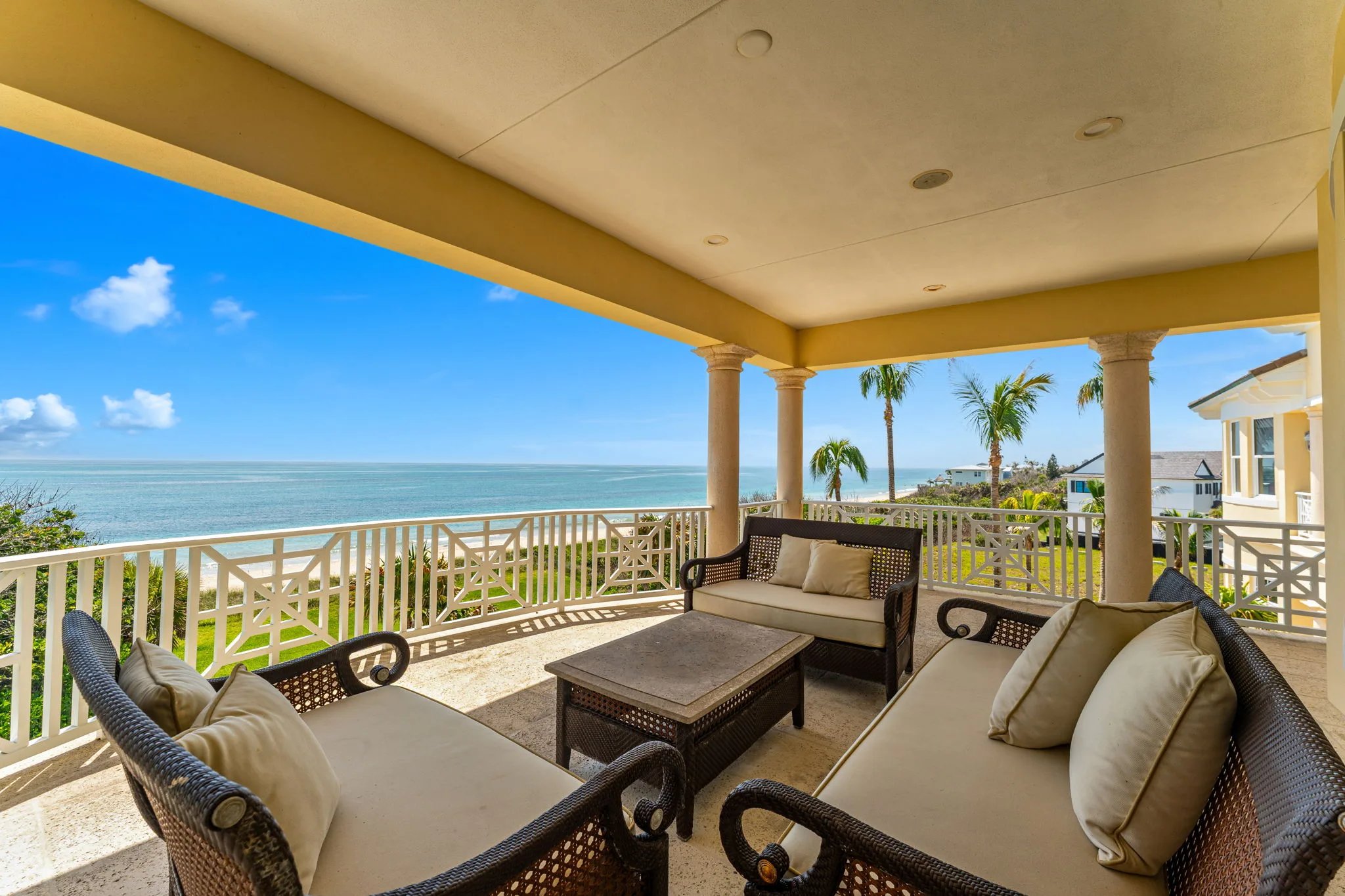 Upper covered porch wicker seating set with ocean horizon beyond Chippendale railing