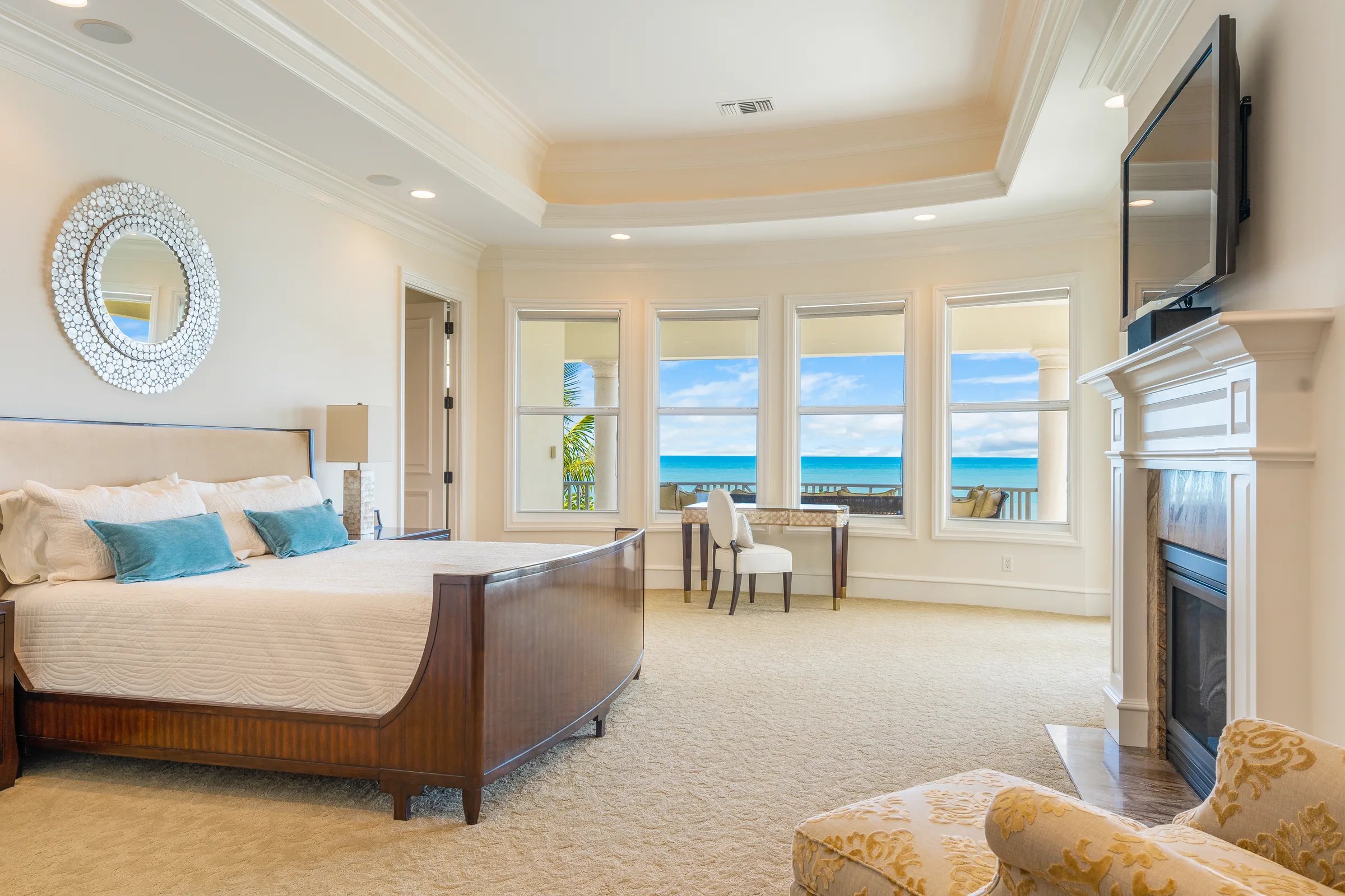 Owner's suite with sleigh king bed, tray ceiling, marble fireplace, and a wall of bay windows opening to the Atlantic