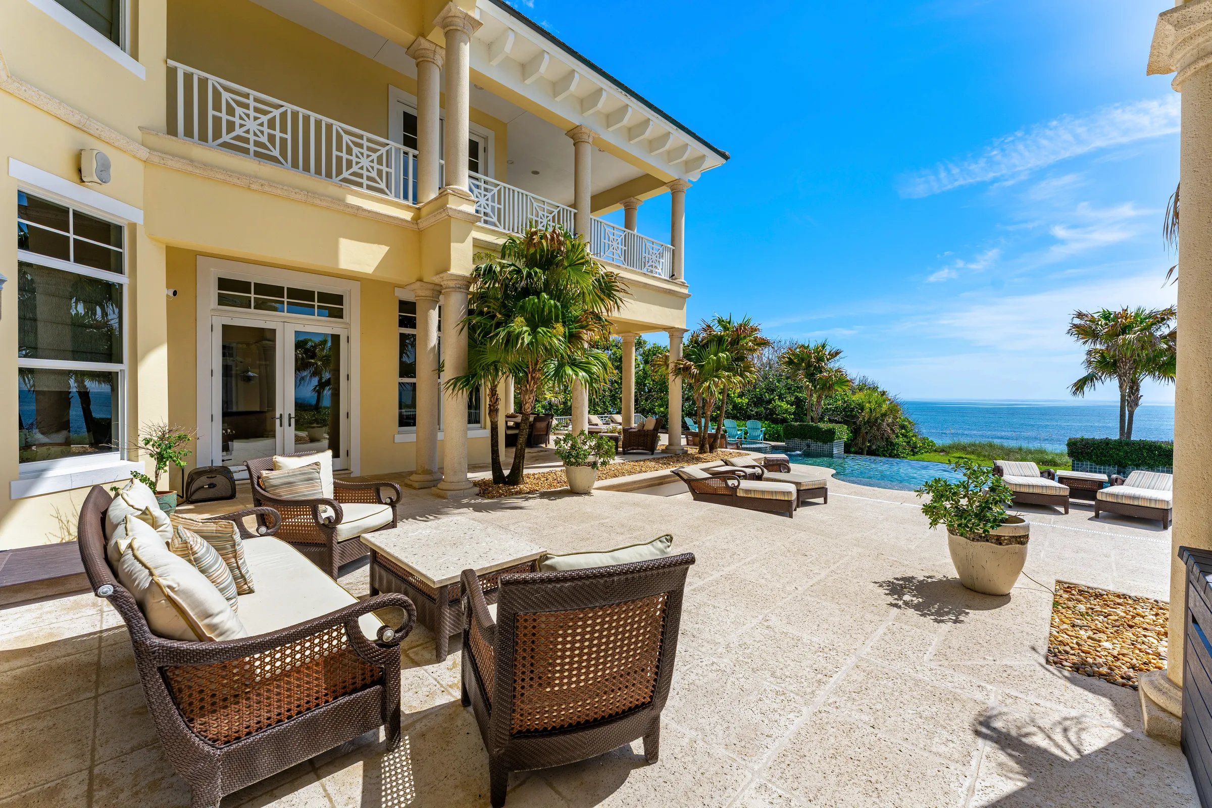 Pool terrace with classical colonnade, wicker lounge seating, and infinity pool overlooking the Atlantic Ocean