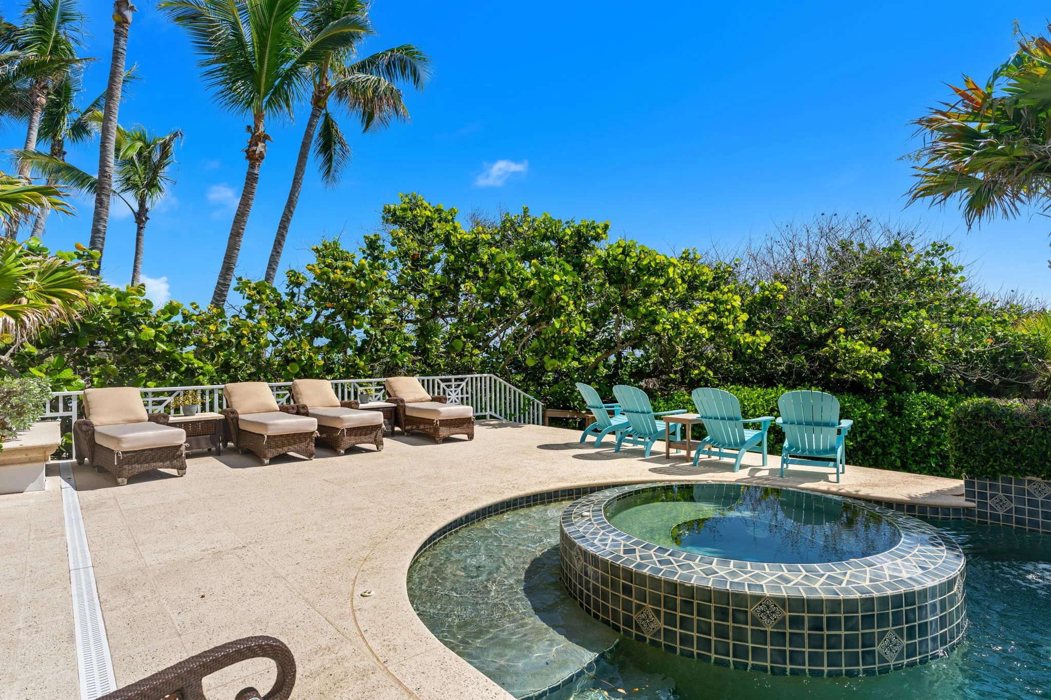 Pool deck lined with wicker chaises and turquoise Adirondacks beside the mosaic spa