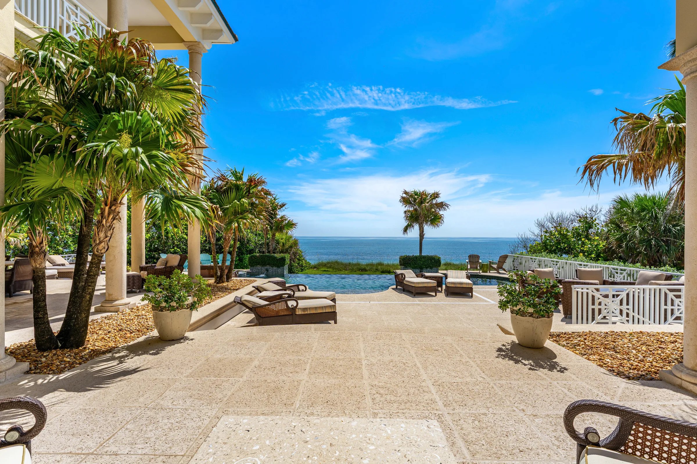 Travertine pool deck with loungers framed by palms opens to infinity pool and Atlantic