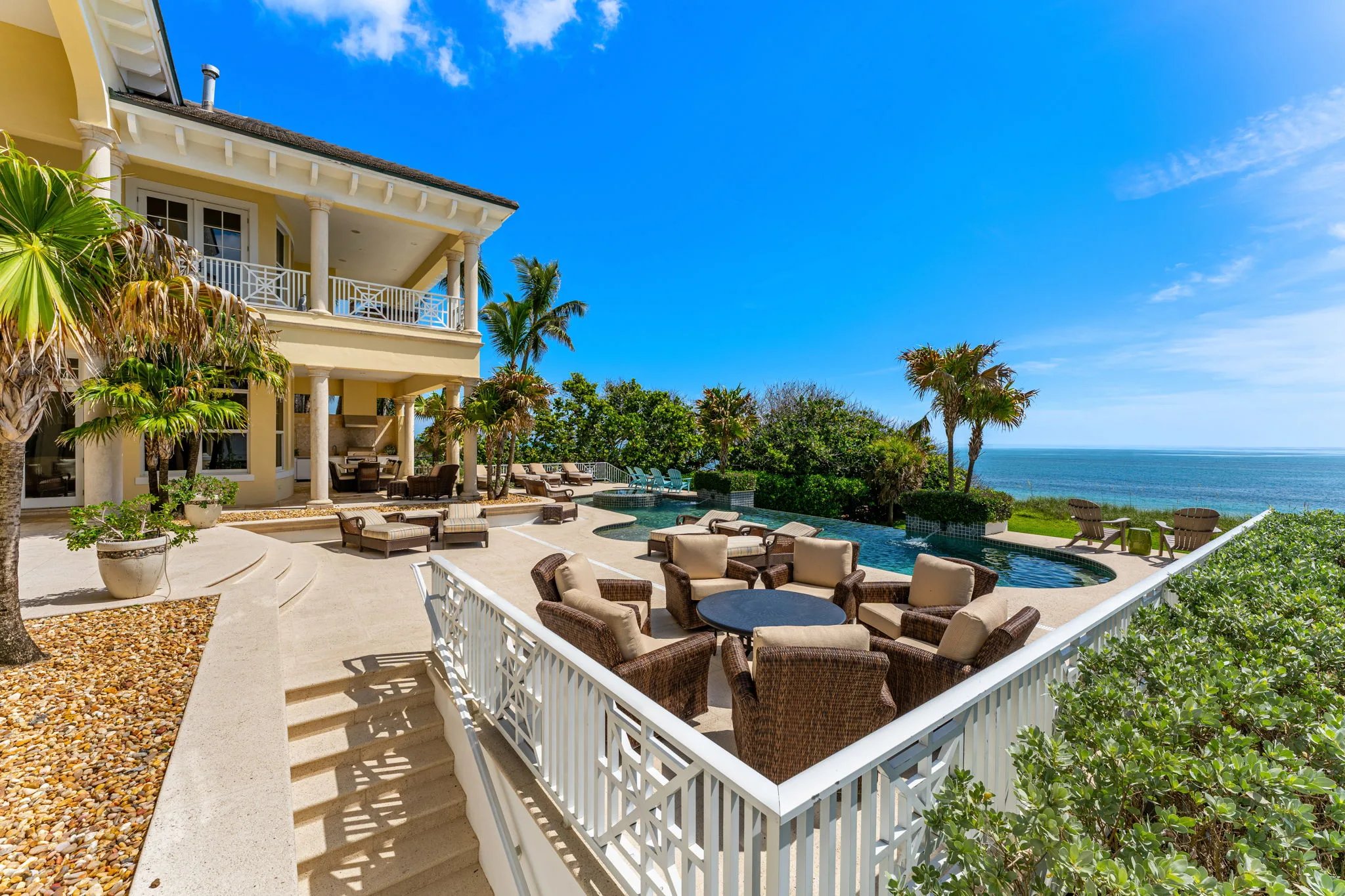Travertine stairs descend to the oceanfront infinity pool deck with seating clusters along the Atlantic edge