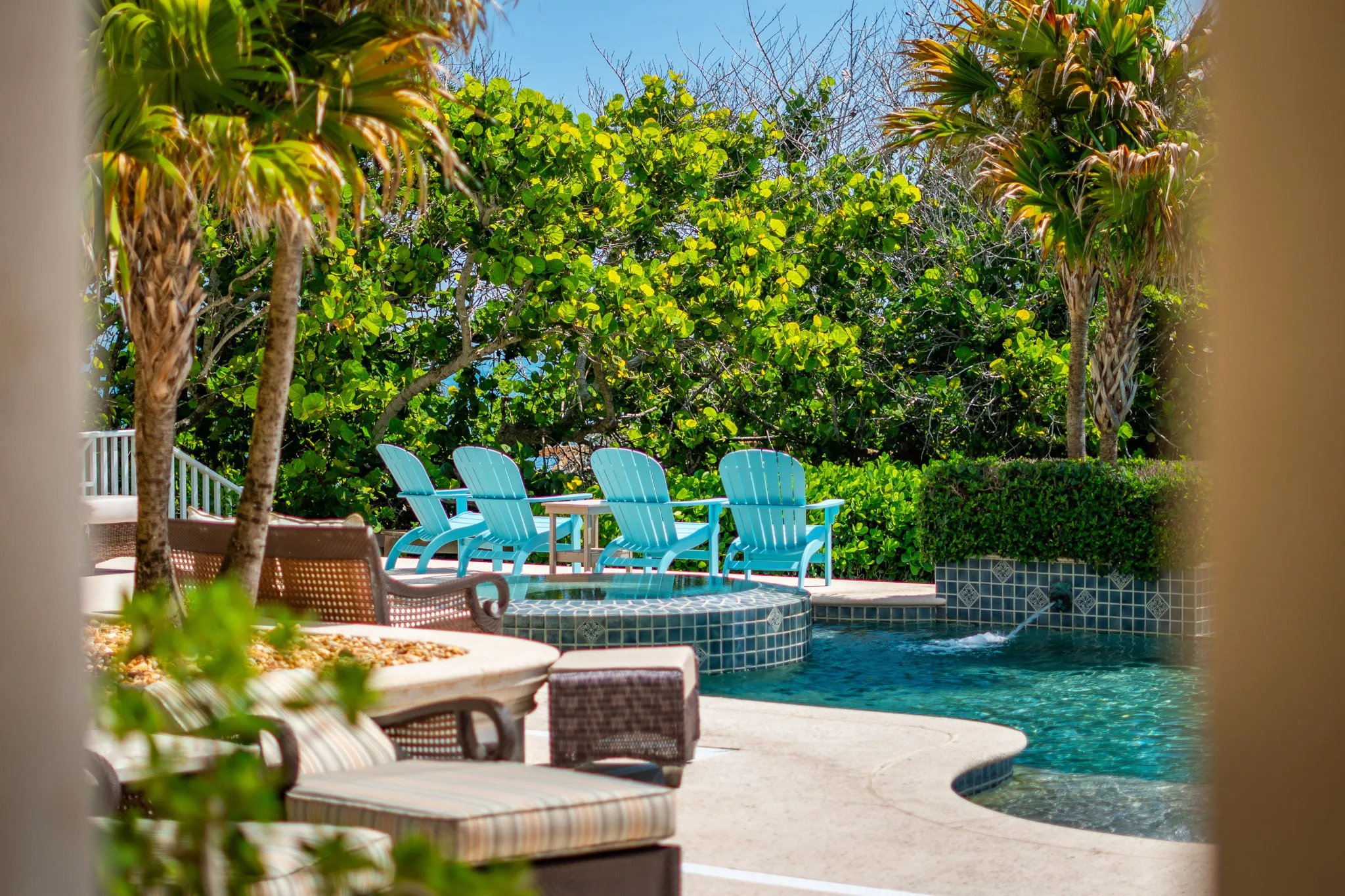 Peek through palms to turquoise Adirondack chairs lining the spa overflow on the oceanfront pool deck