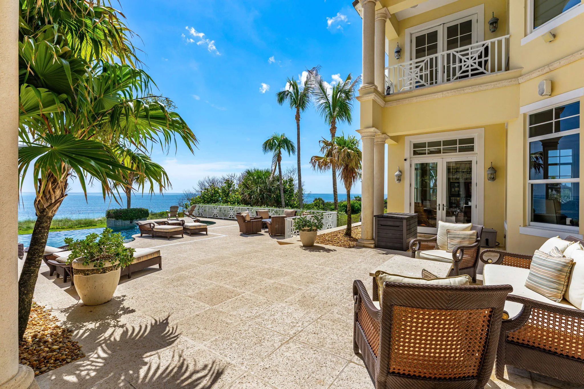 Travertine pool terrace with chaise loungers, wicker seating and infinity edge toward the Atlantic