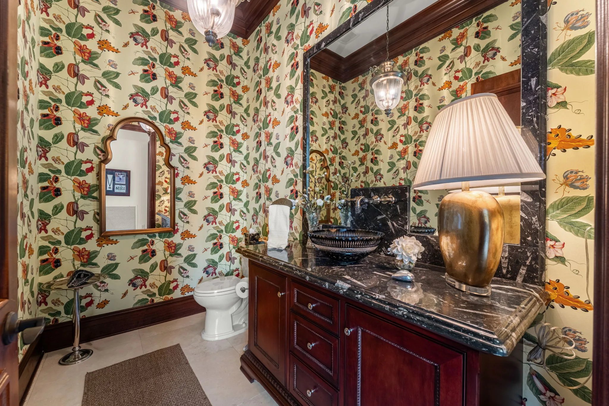 Powder room cloaked in botanical hibiscus wallpaper with marble vanity, mahogany cabinetry and brass fittings