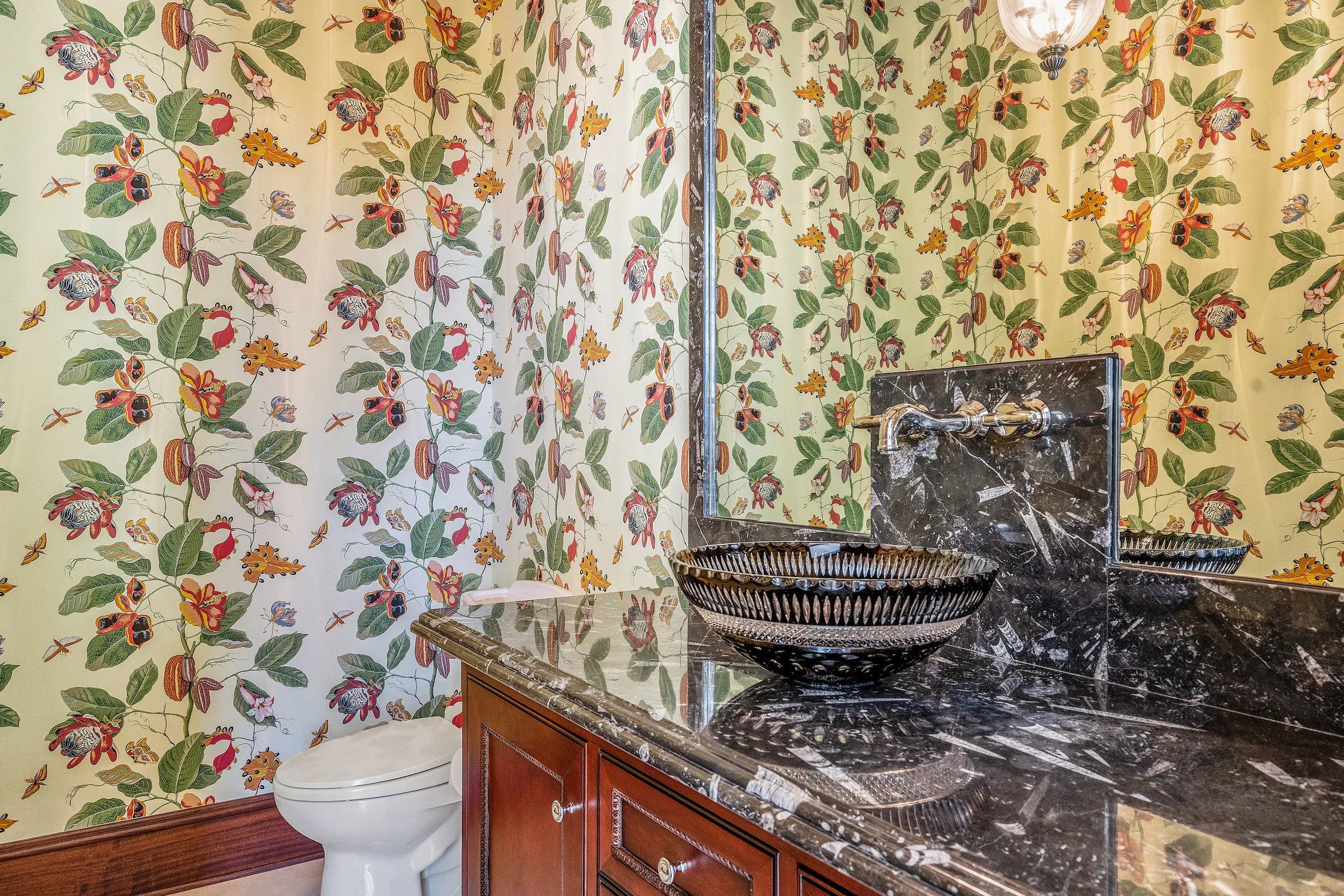 Powder room with bold botanical wallpaper, dark marble vanity, and a striped vessel sink