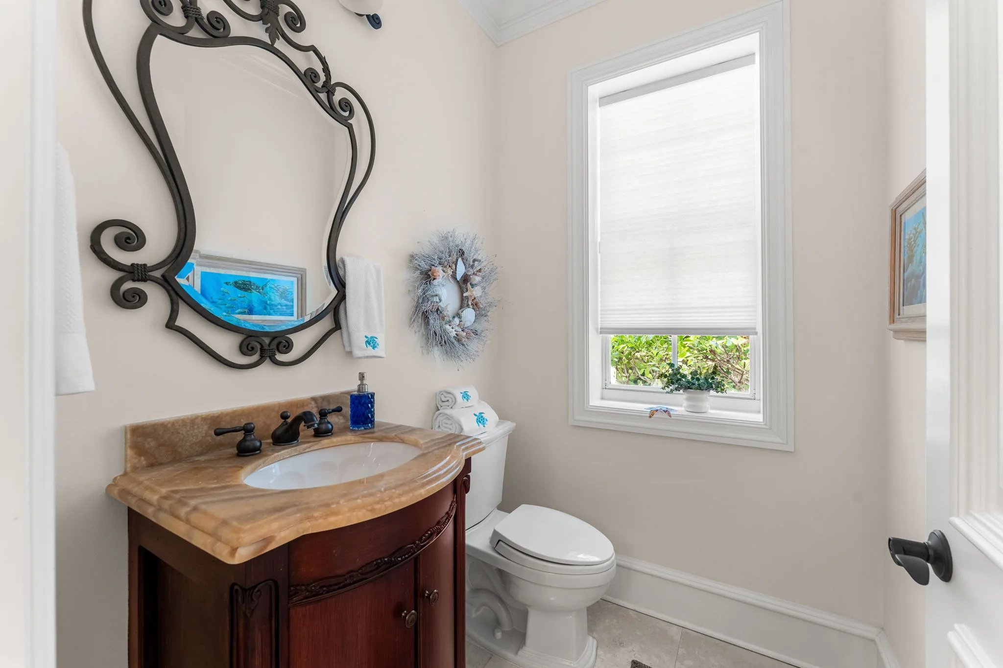Powder room with ornate wrought-iron mirror, onyx vanity and shell-coastal wreath