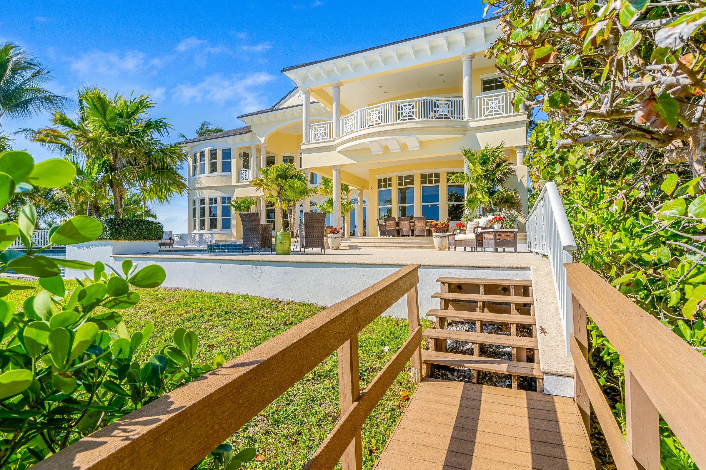 Wide view of the rear facade and lanai from the boardwalk side, with sea grape framing the path back to the house