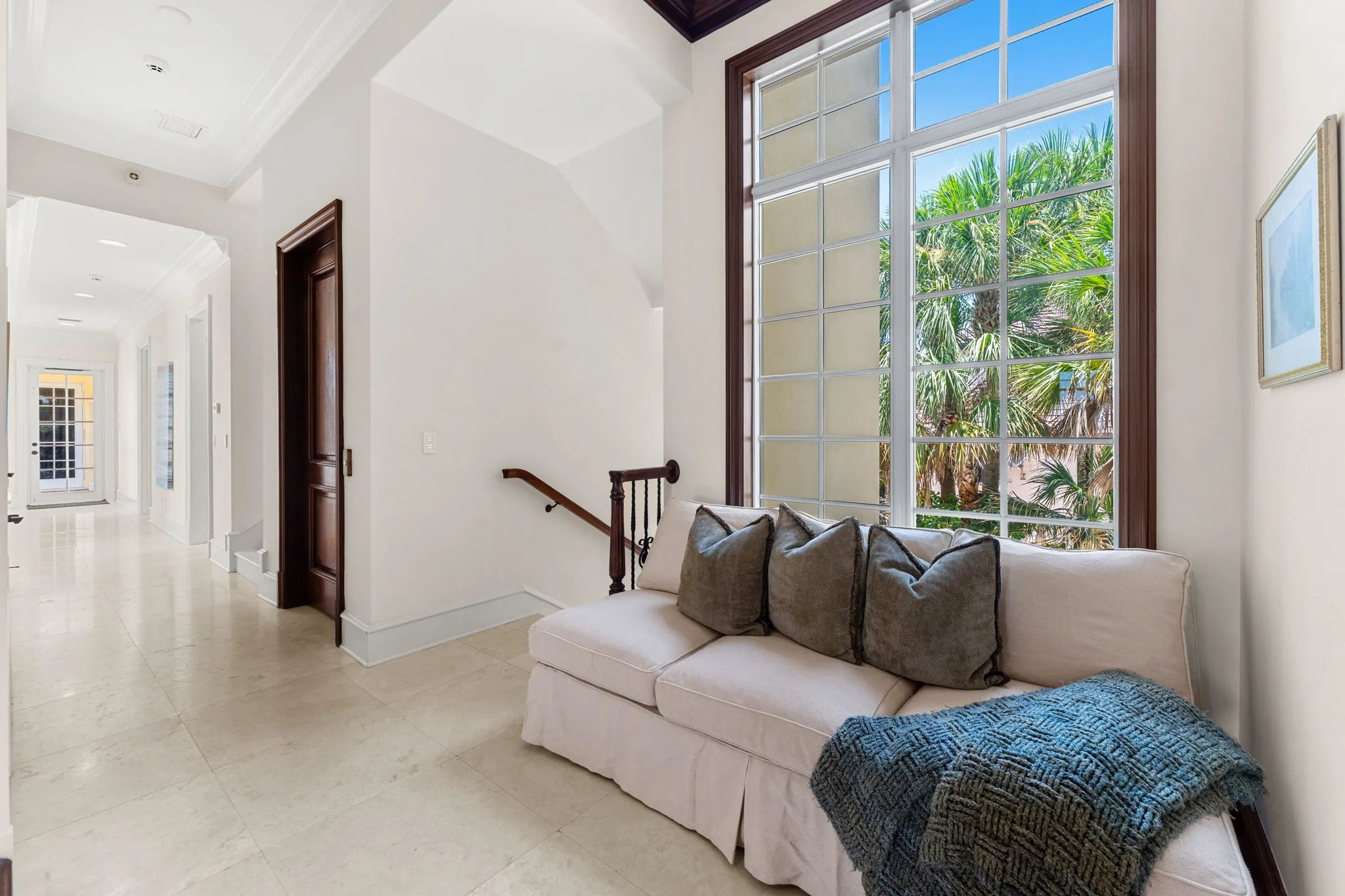 Stair landing reading nook with linen sofa beneath a tall mullioned palm-framed window