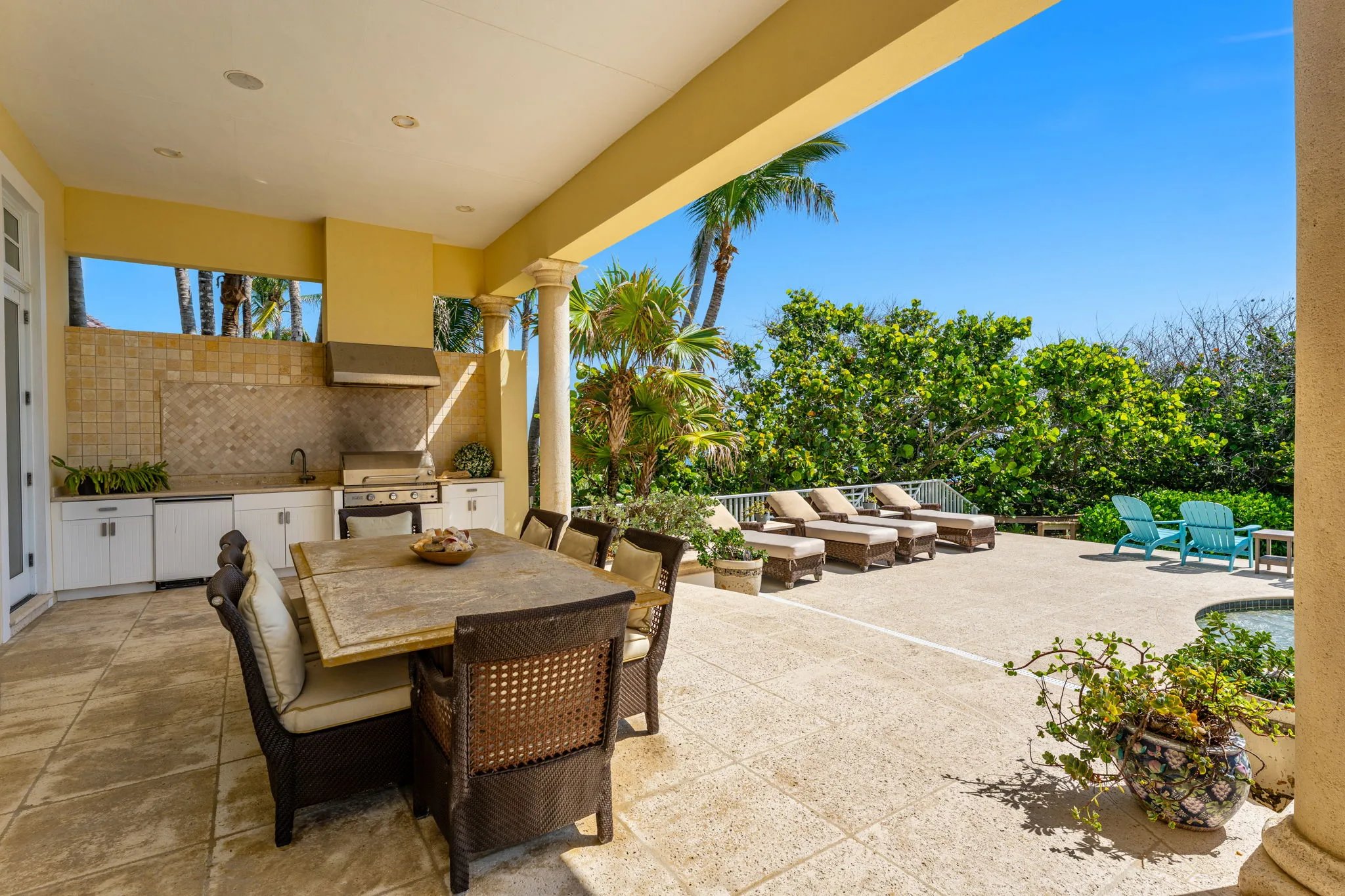 Covered summer kitchen with grill, dining table, and view past chaises to dune